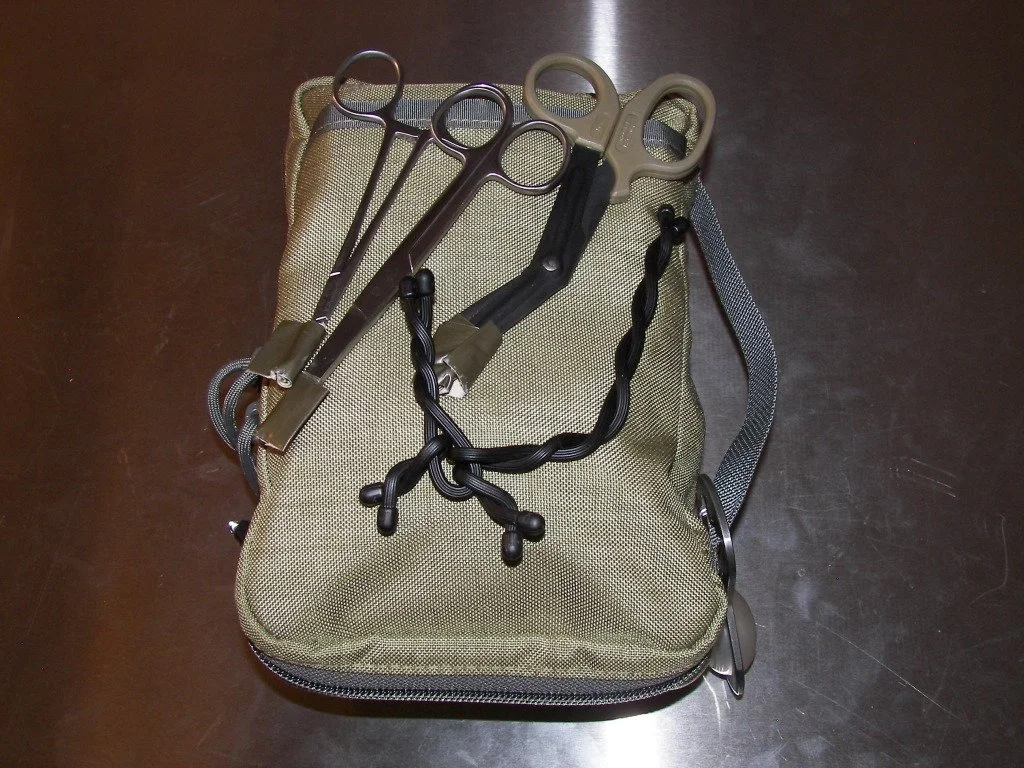 Tactical medical kit with scissors and forceps on metal surface.