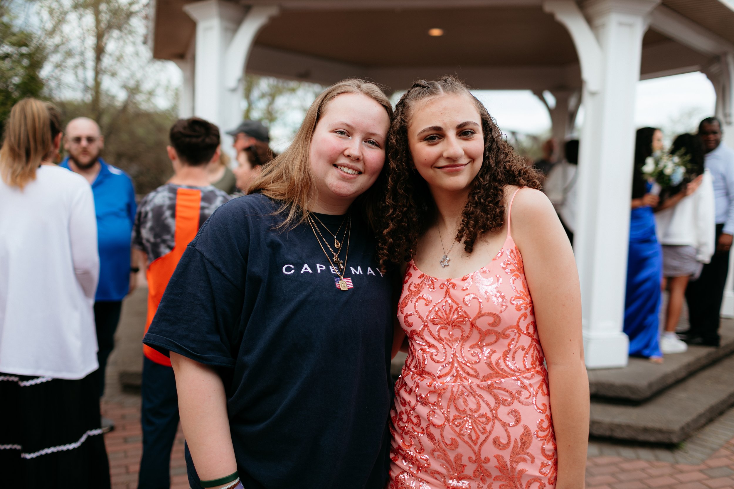 Two people smiling at an outdoor event, one wearing a dark t-shirt and the other in a sequin dress.
