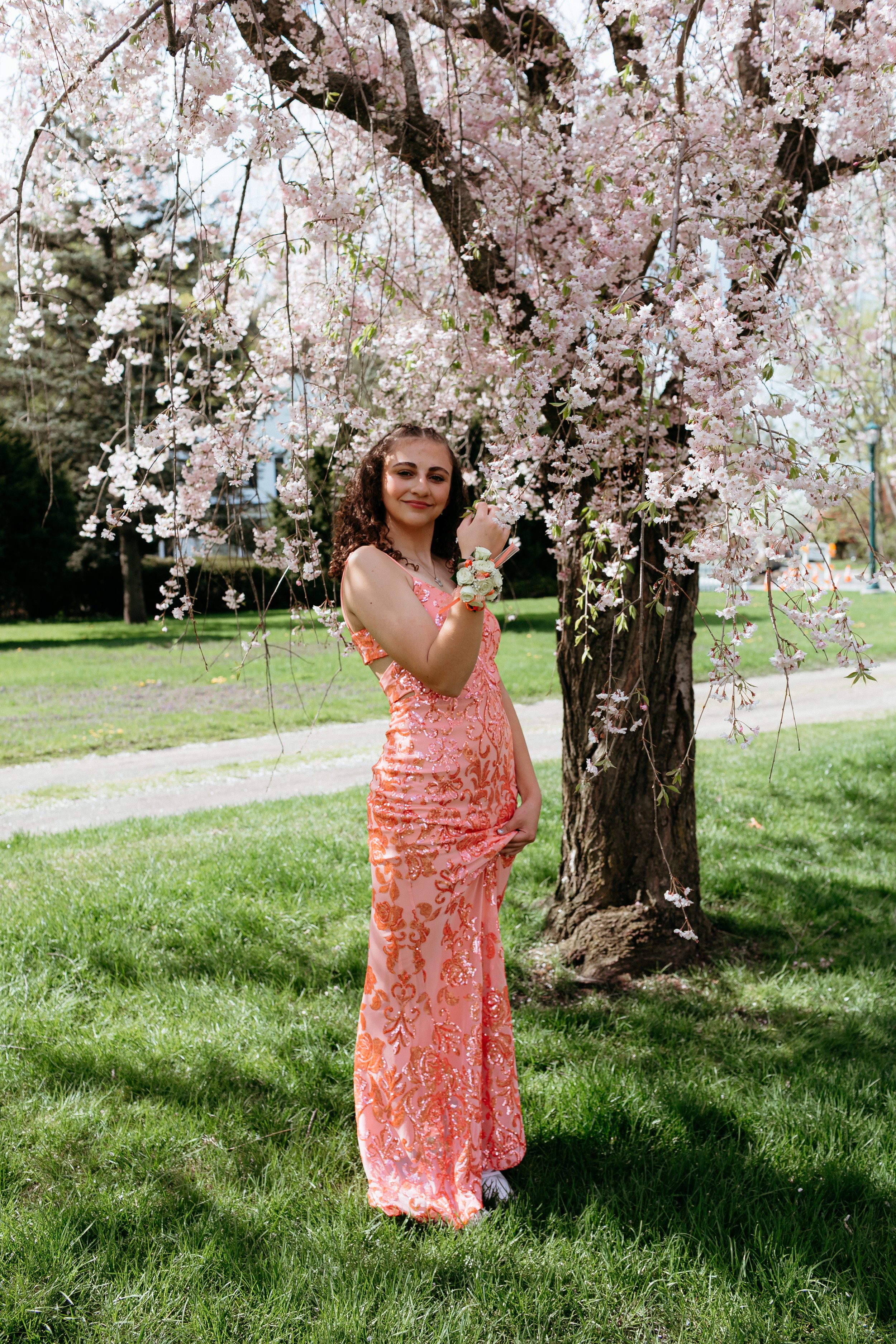 Young woman in an orange floral dress under a cherry blossom tree