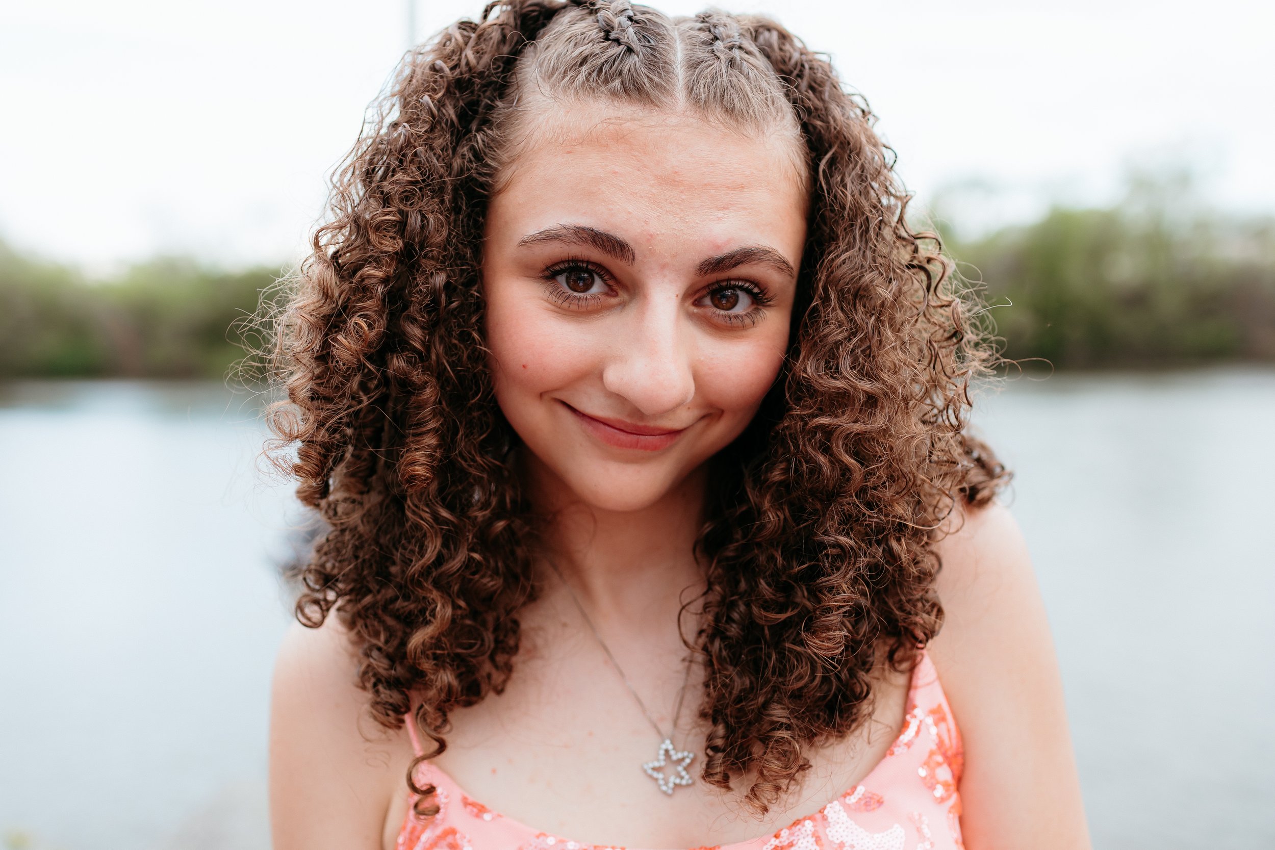 Girl with curly hair smiling at camera outdoors.