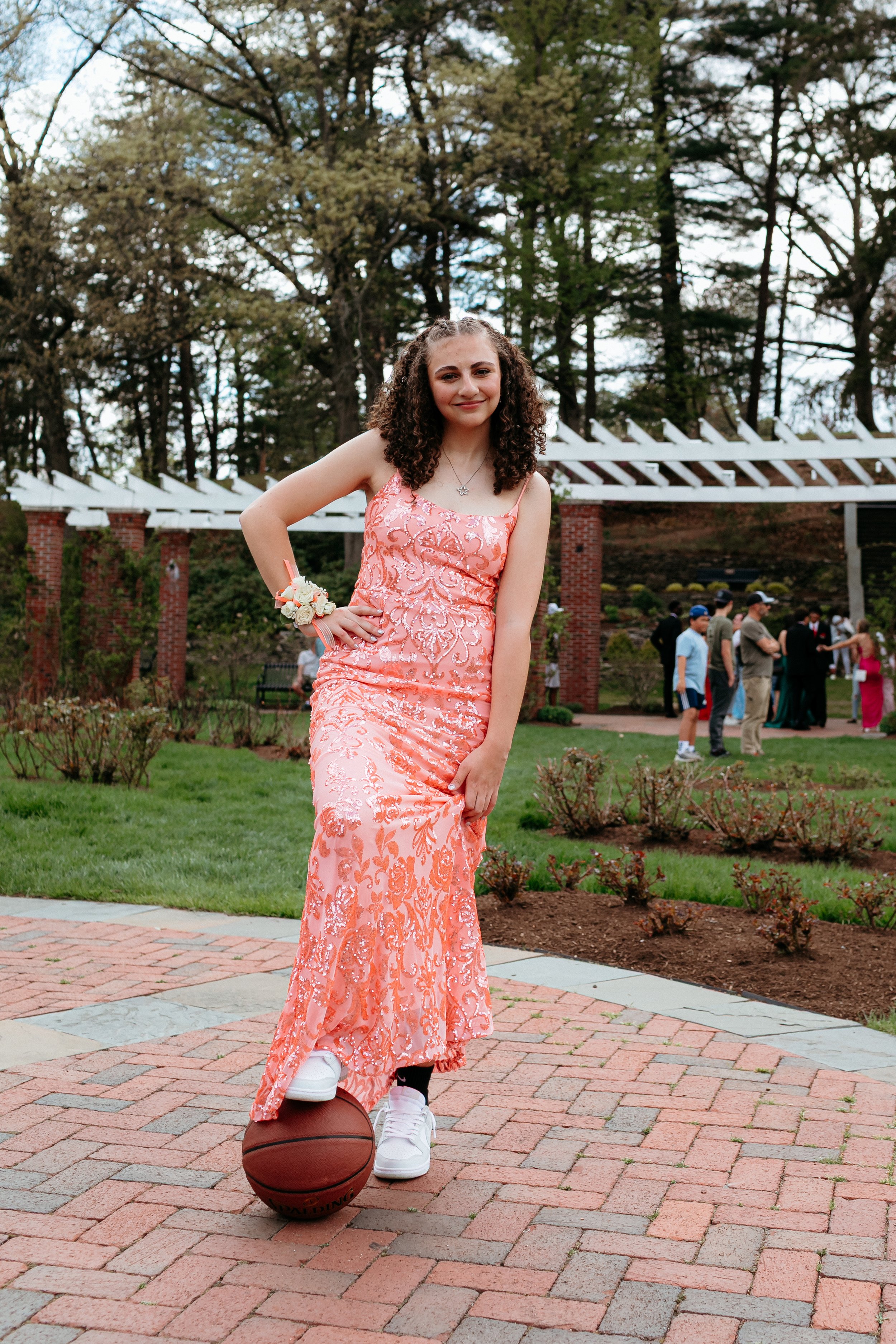 Teen girl in a pink dress and sneakers, with a basketball, posing outdoors.