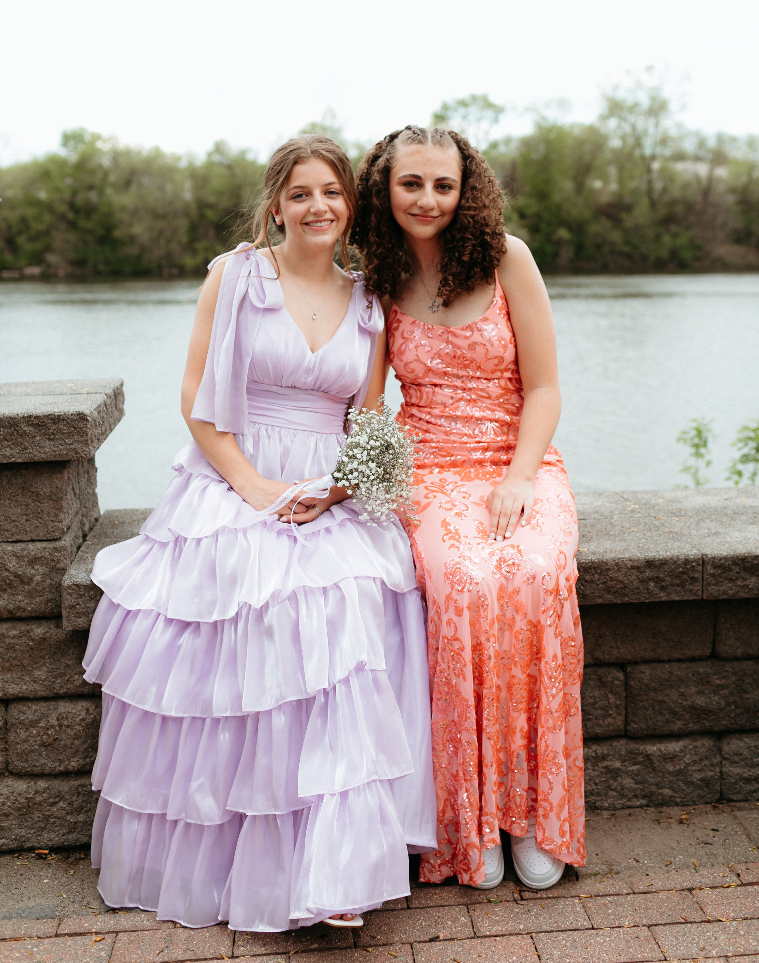 Two women in formal dresses sitting on a stone bench by a river.