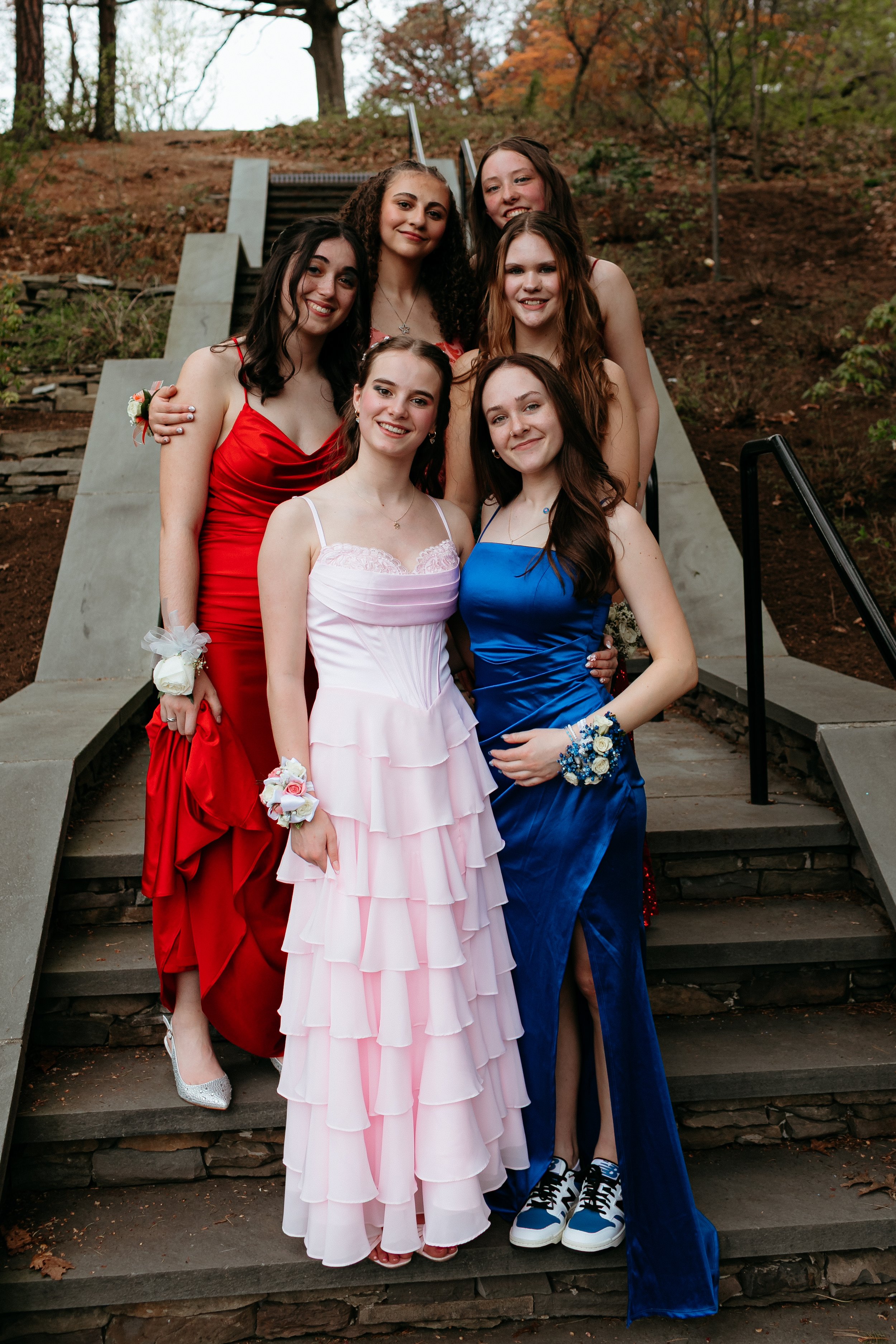 Group of young women in colorful formal dresses standing on outdoor stairs, wearing corsages.