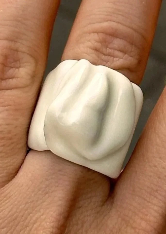 Close-up of a hand wearing a large, white, sculptural ring with a textured, organic surface.