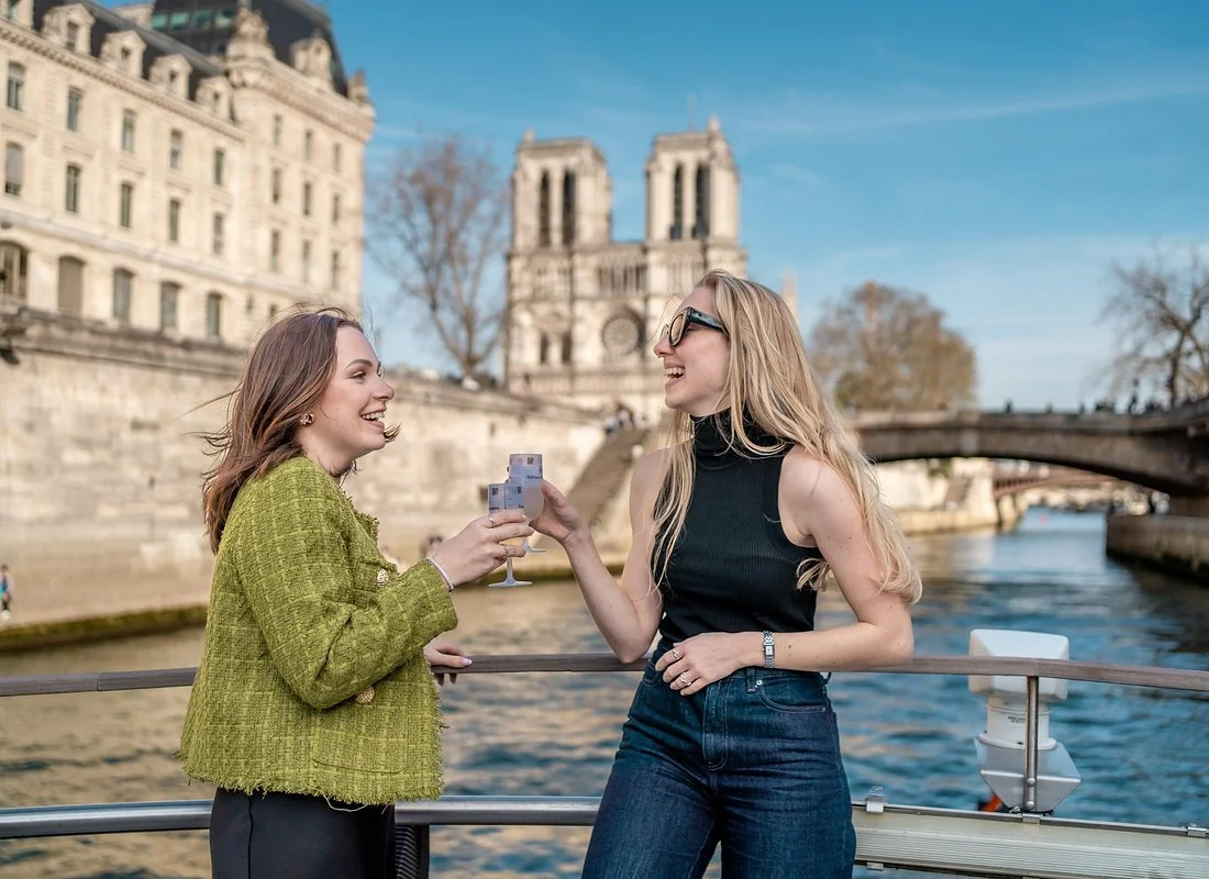 Interior of a restaurant with large windows overlooking a river and cityscape at dusk, tables set with glassware and candles.