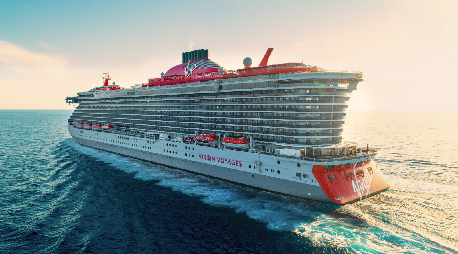 A large cruise ship sailing on the ocean at sunset, with the logo 'Virgin Voyages' visible on the side and top of the ship.