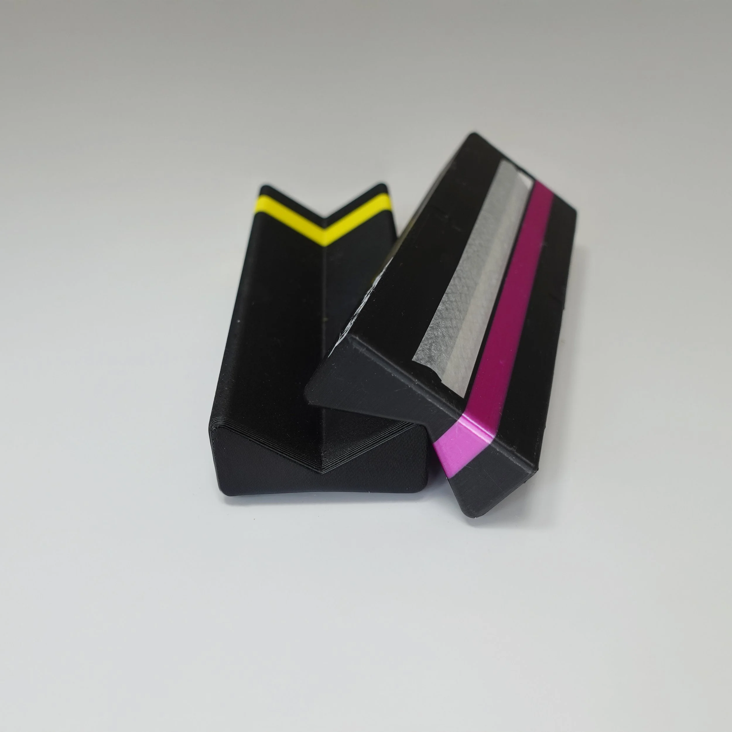 Two ZigaJig King Slim Rolling Racks one with yellow and black stripes, the other with pink and black stripes, placed on a white surface.