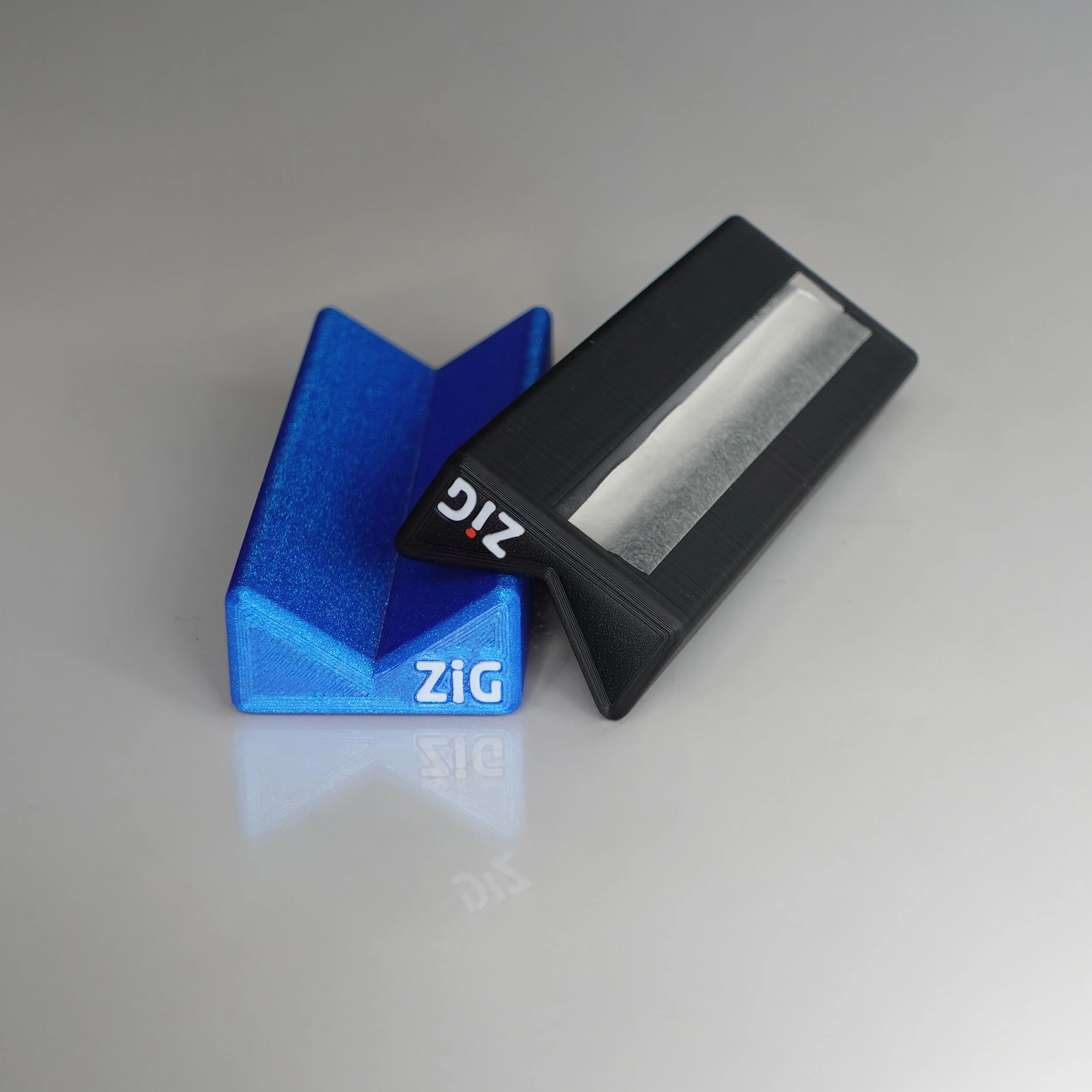 A black and a blue 3D-printed ZigaJig King Slim Rolling Rack on a gray surface.