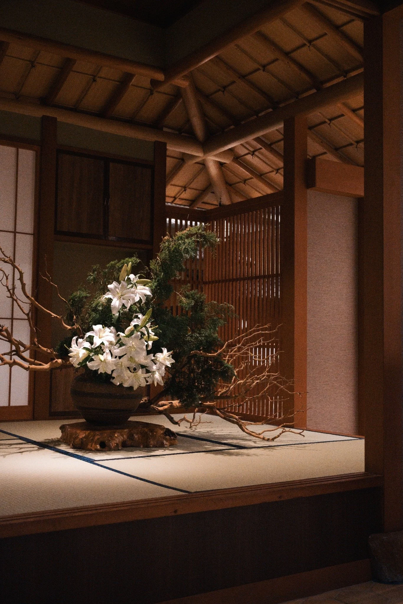 White lilies and branches in a warm wood interior with tatami flooring