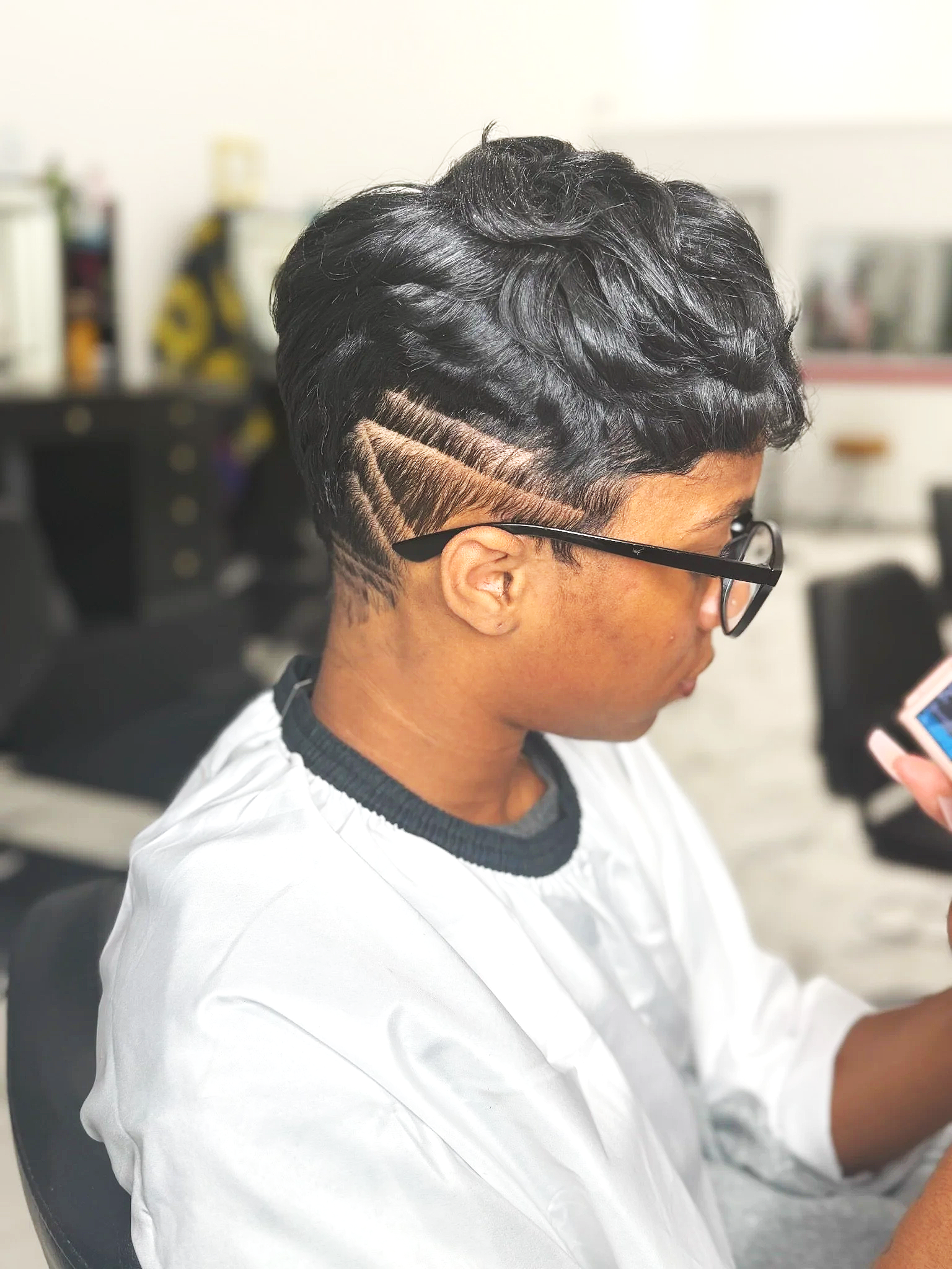 A woman with short, dark, wavy hair sporting a shaved side with a geometric patterned design.