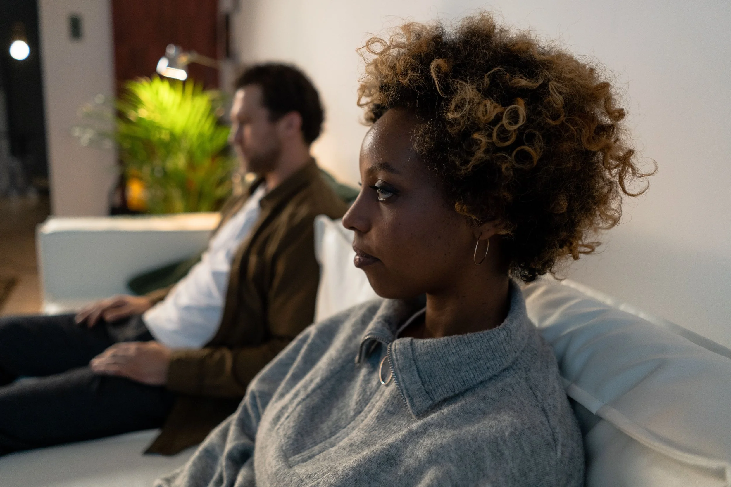 Couple sitting together on a couch but emotionally distant, feeling like housemates instead of partners