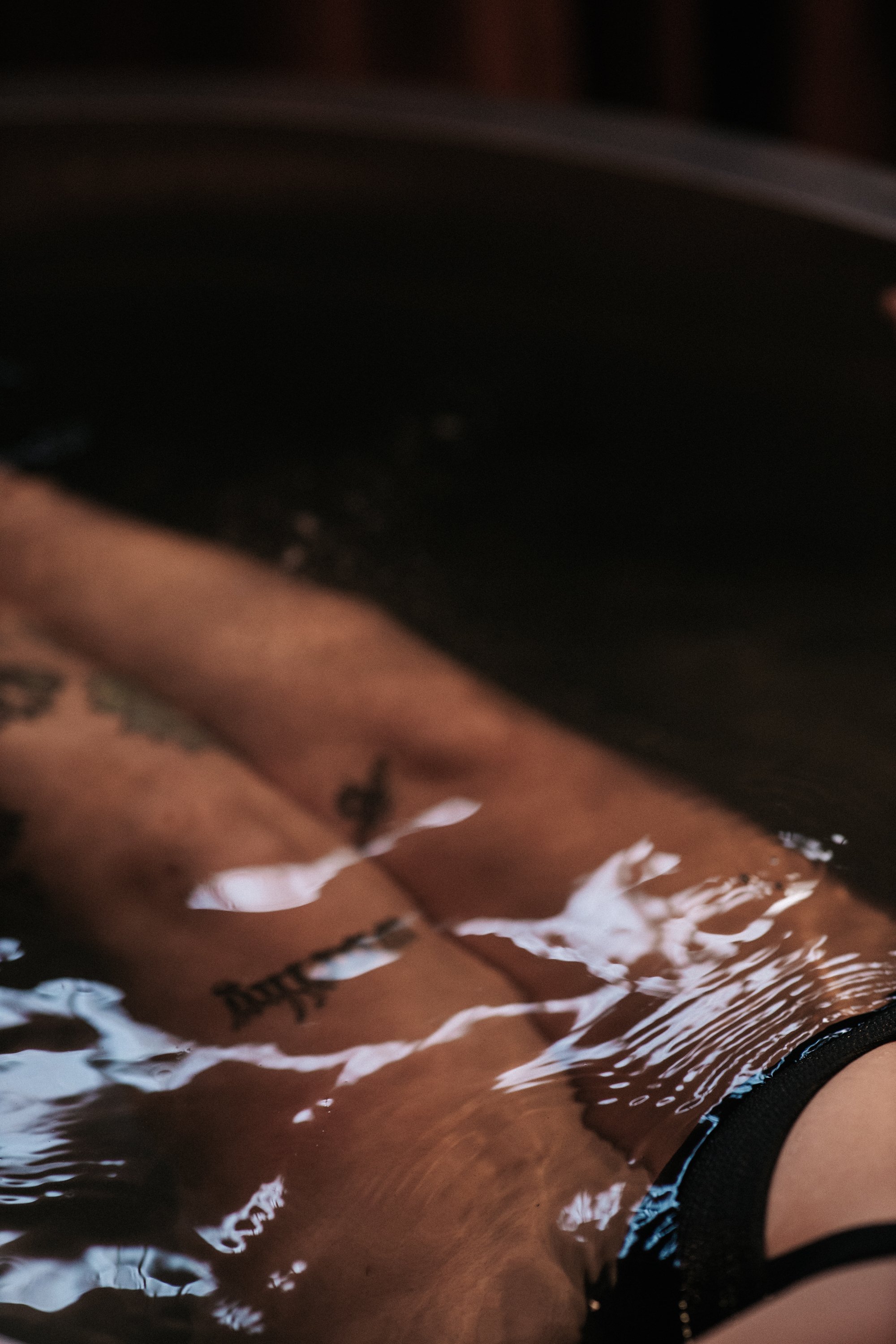 Close-up of a person's forearm with tattoos, submerged in water, with reflections on the water's surface.