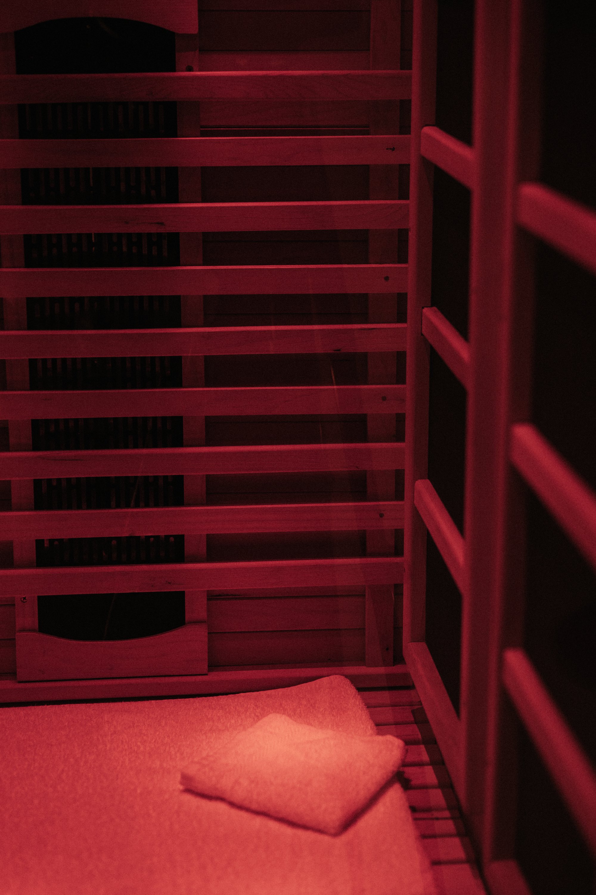 A wooden bunk bed with a ladder, illuminated by red light, with a beige blanket folded at the foot of the bed.