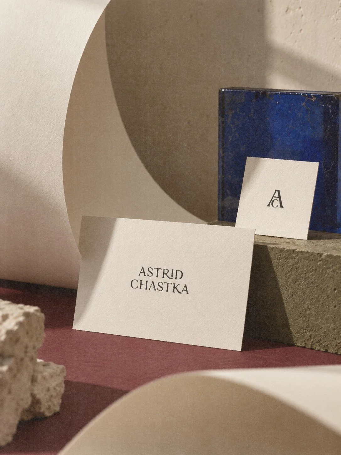A name card with the name 'Astrid Chastka' and a small card with the letter 'A' on a blue box in a display with textured stones and paper backgrounds.