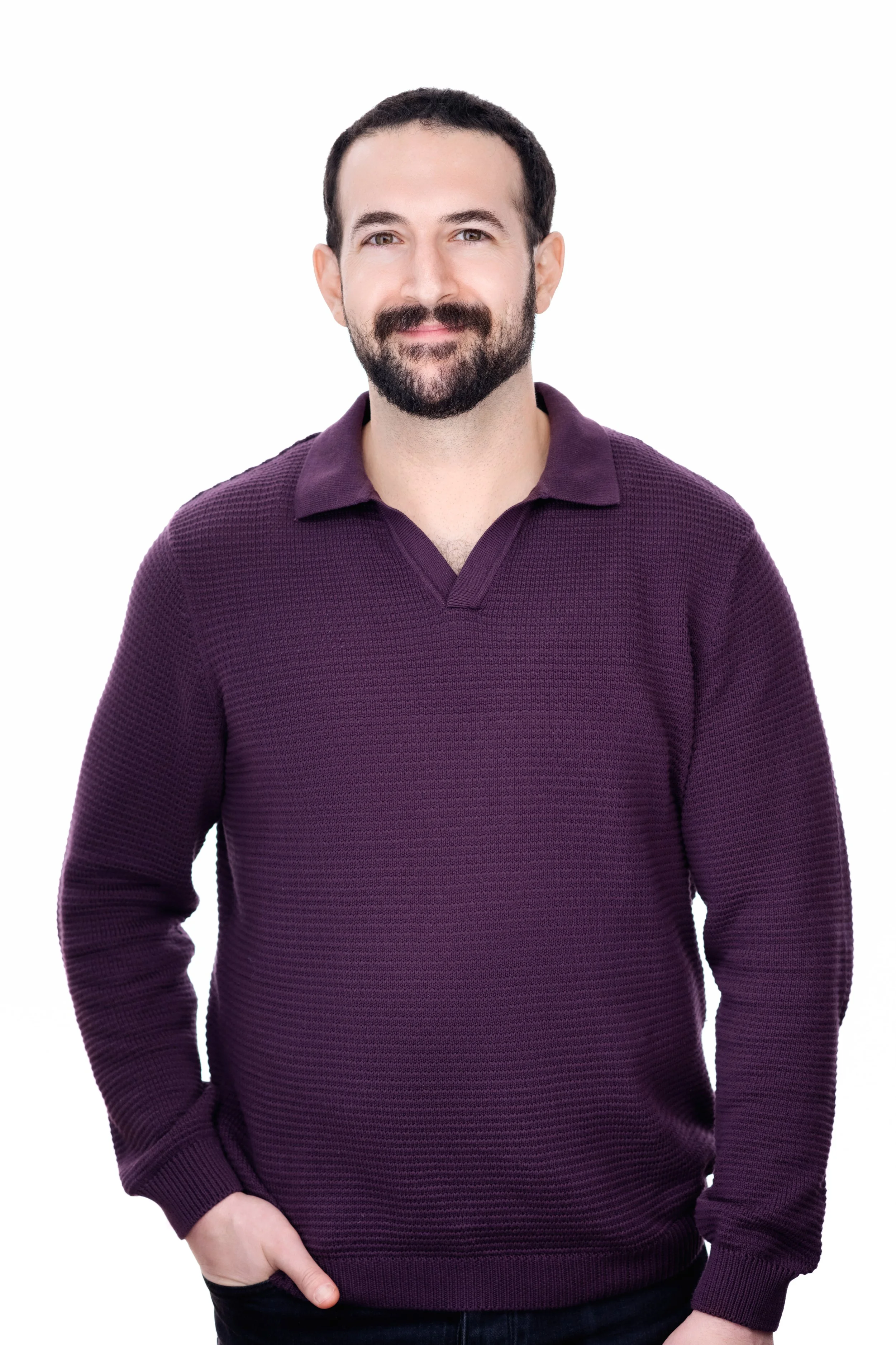 A man with a beard and short dark hair wearing a purple textured long-sleeve polo shirt, standing against a plain white background.