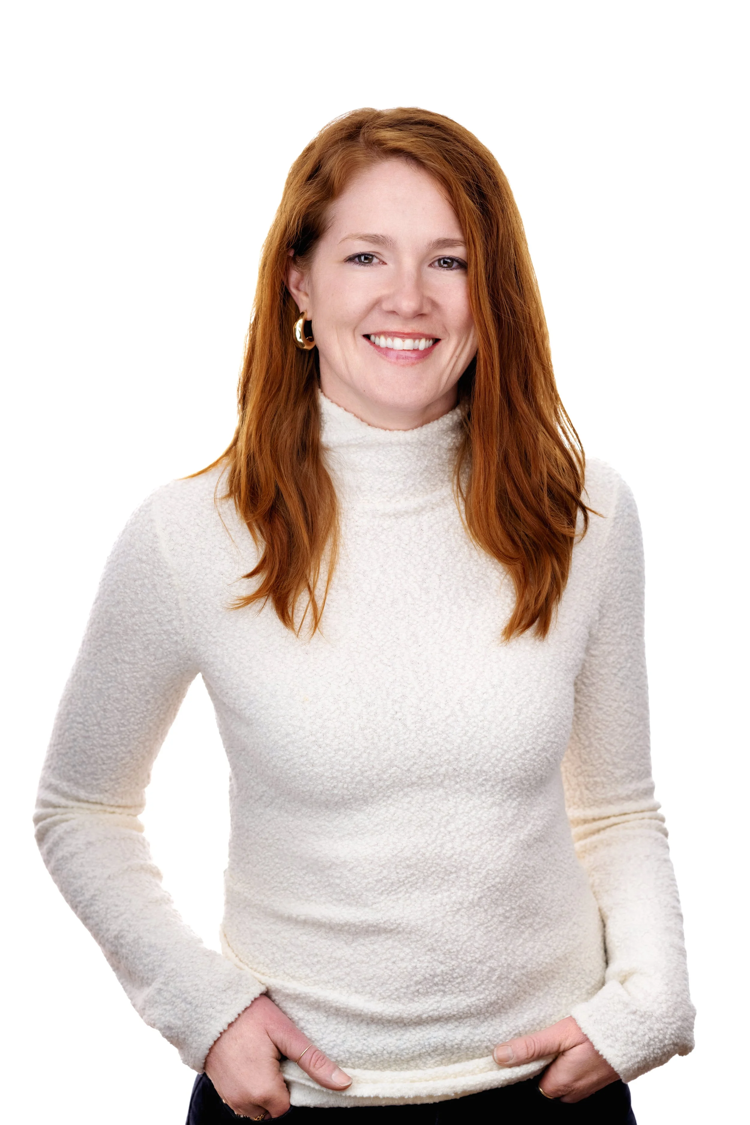 A woman with red hair wearing a cream-colored sweater and gold hoop earrings, smiling against a white background.