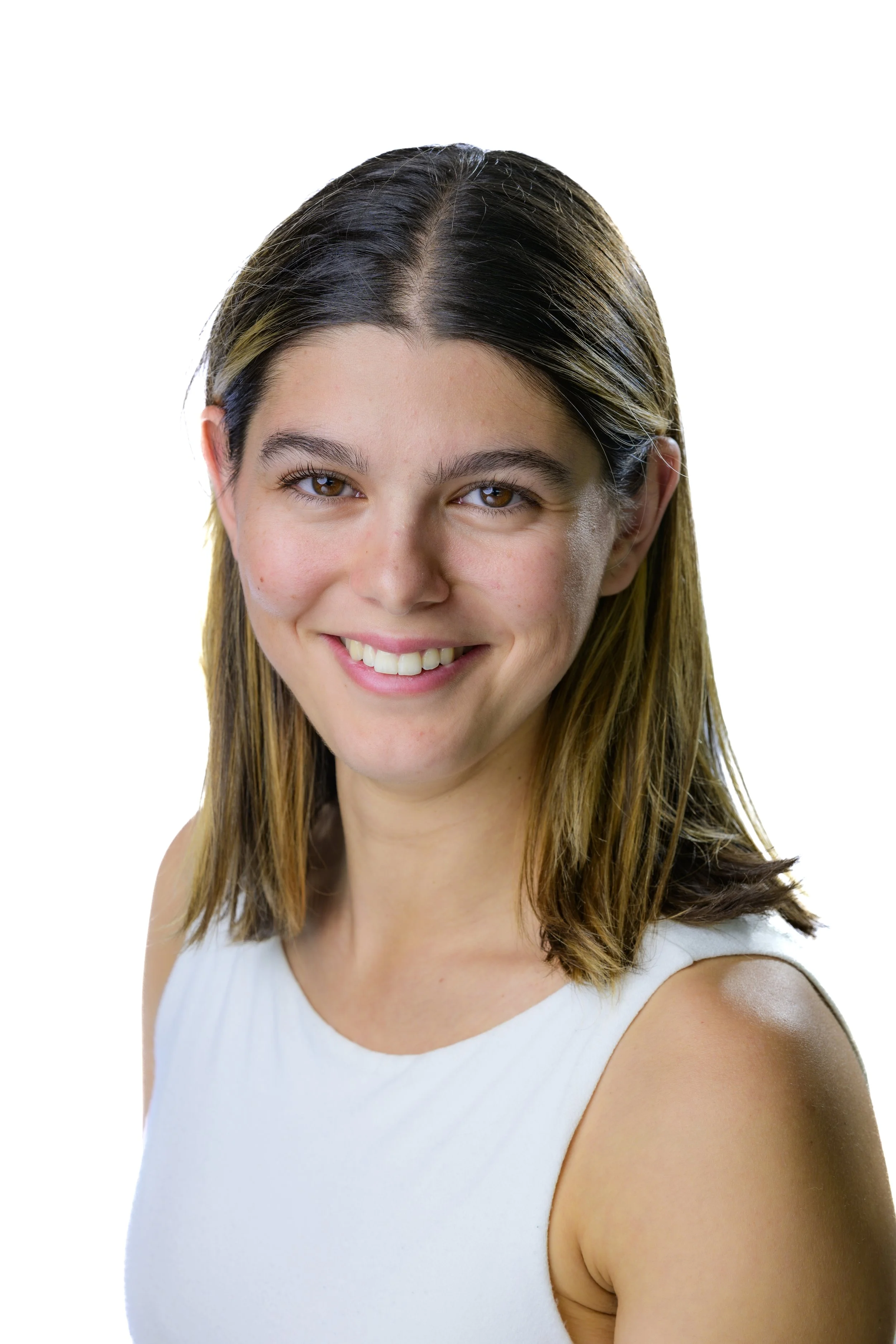 Portrait of a young woman with shoulder-length brown hair, smiling, wearing a sleeveless white top, against a plain white background.