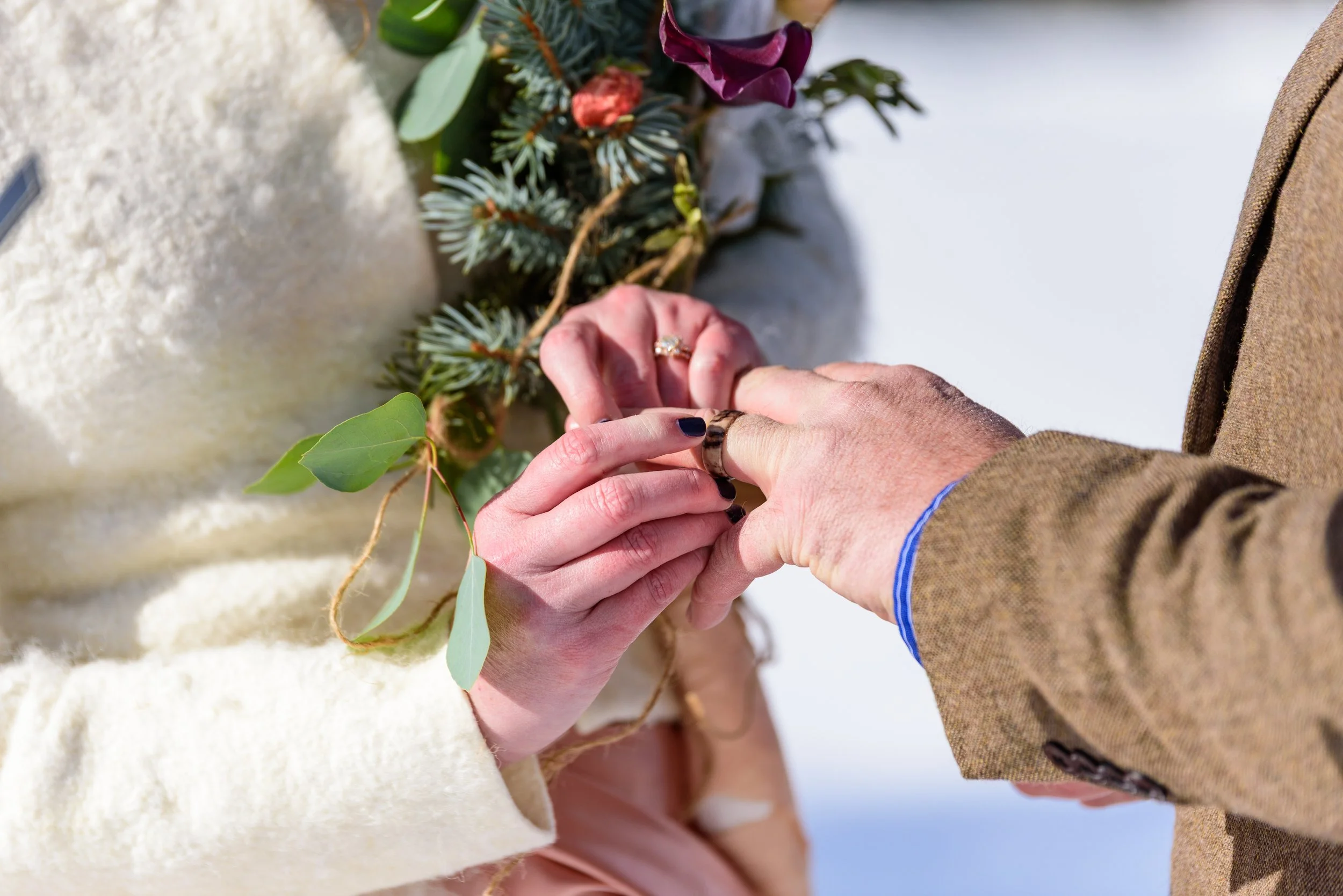 Close-up of a couple exchanging rings during a wedding ceremony, with a floral arrangement behind them.