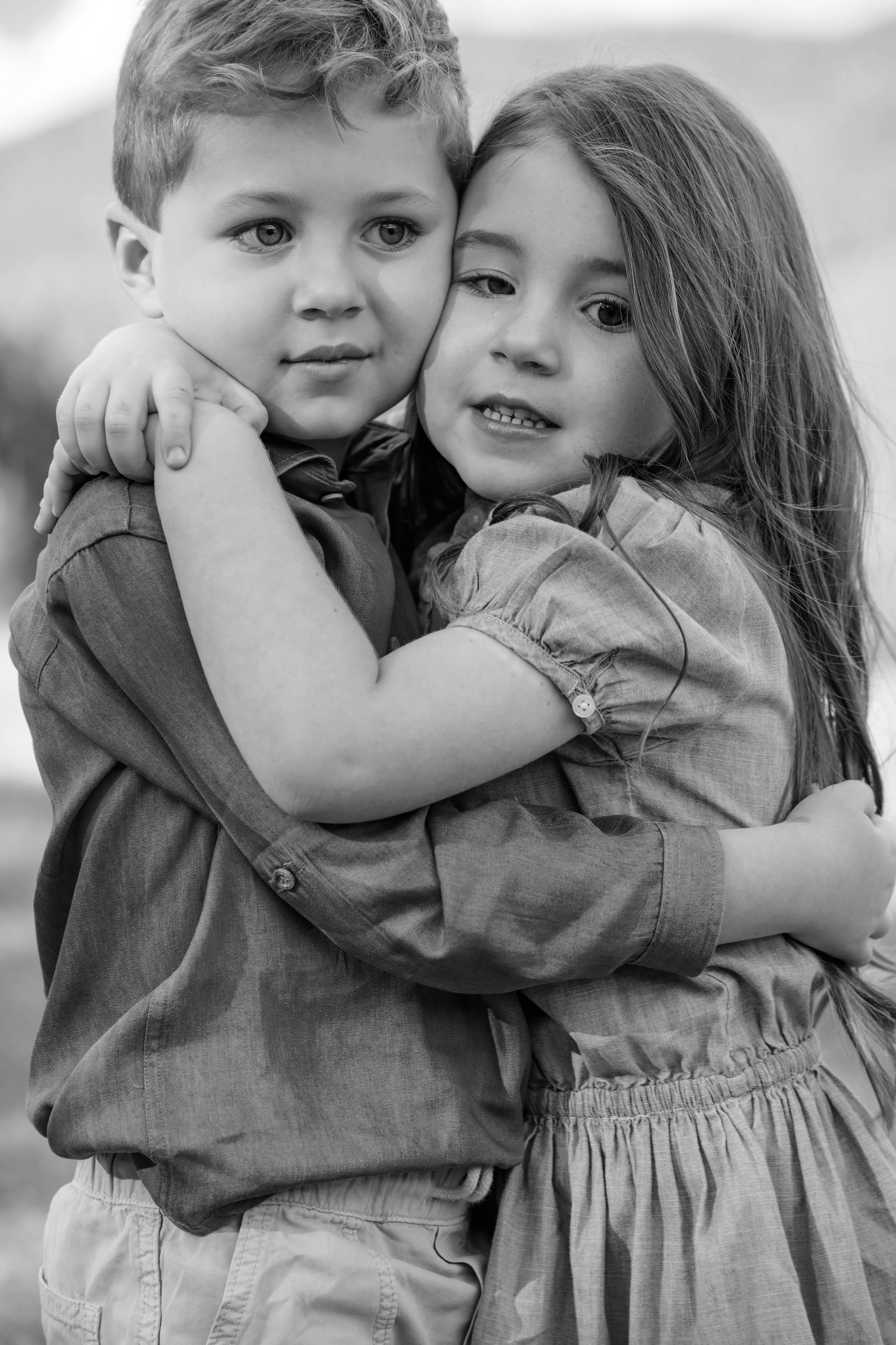 Black and white photo of two children hugging each other, a boy and a girl, outdoors.
