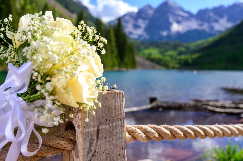 Yellow and white flower bouquet on a wooden post with a scenic mountain lake background.