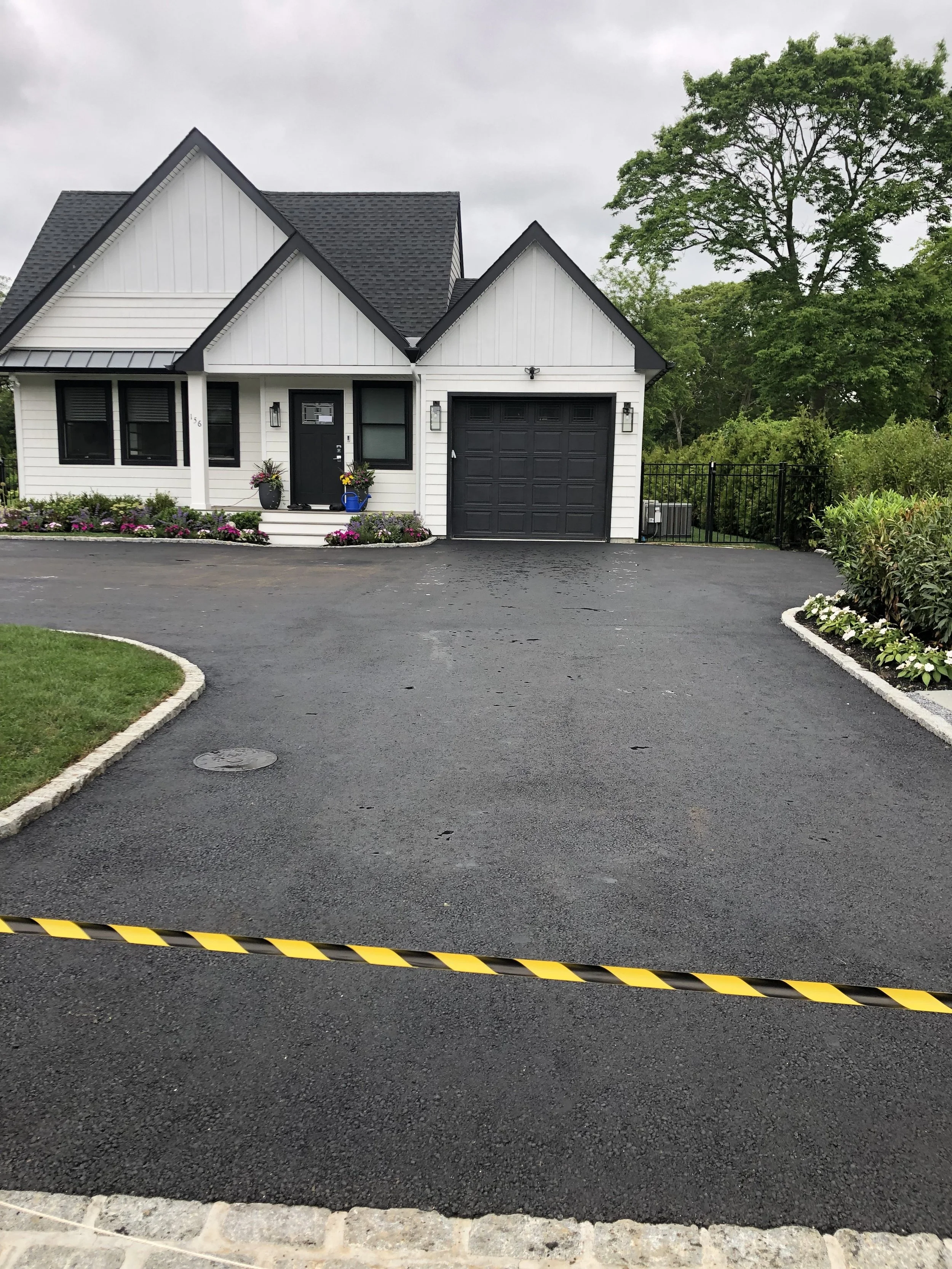 House with gray roof, asphalt driveway, and garage; yellow and black striped caution tape across driveway.