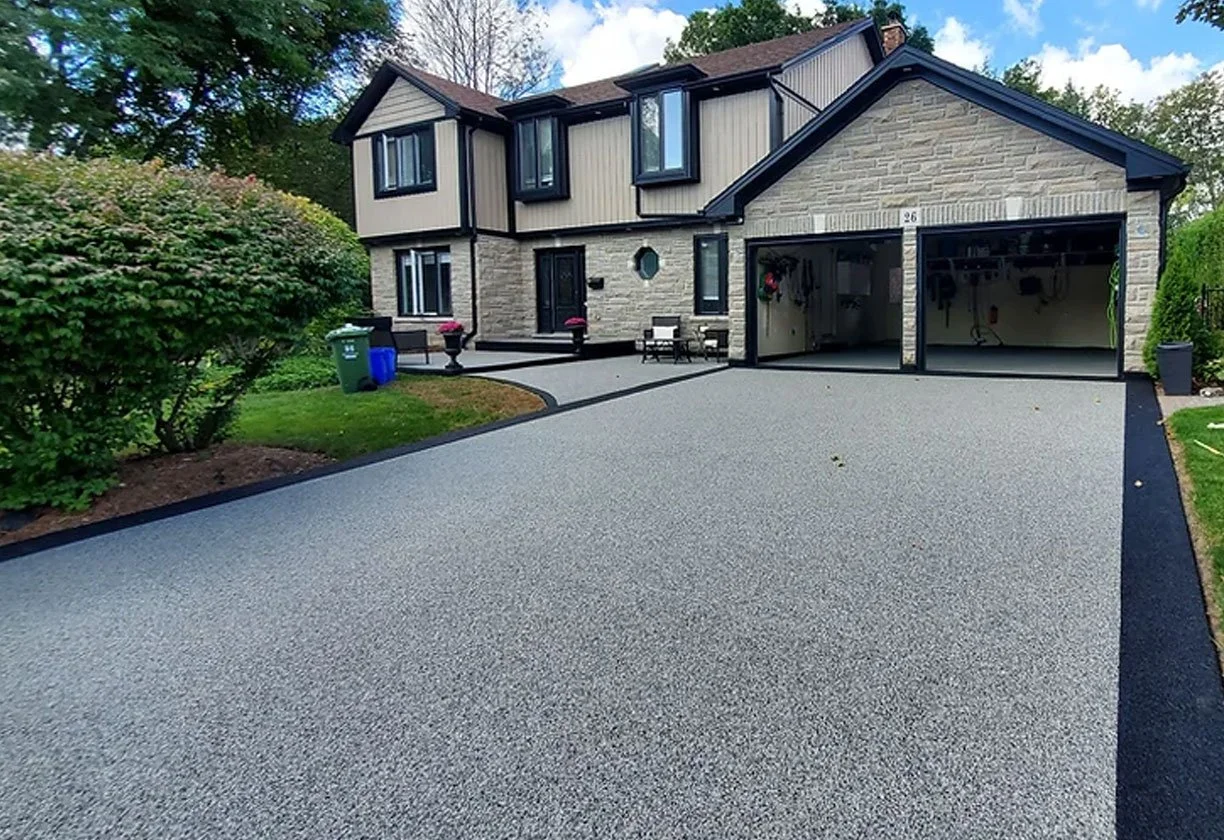 Two-story house with a newly paved driveway, open garage doors, and surrounding greenery.