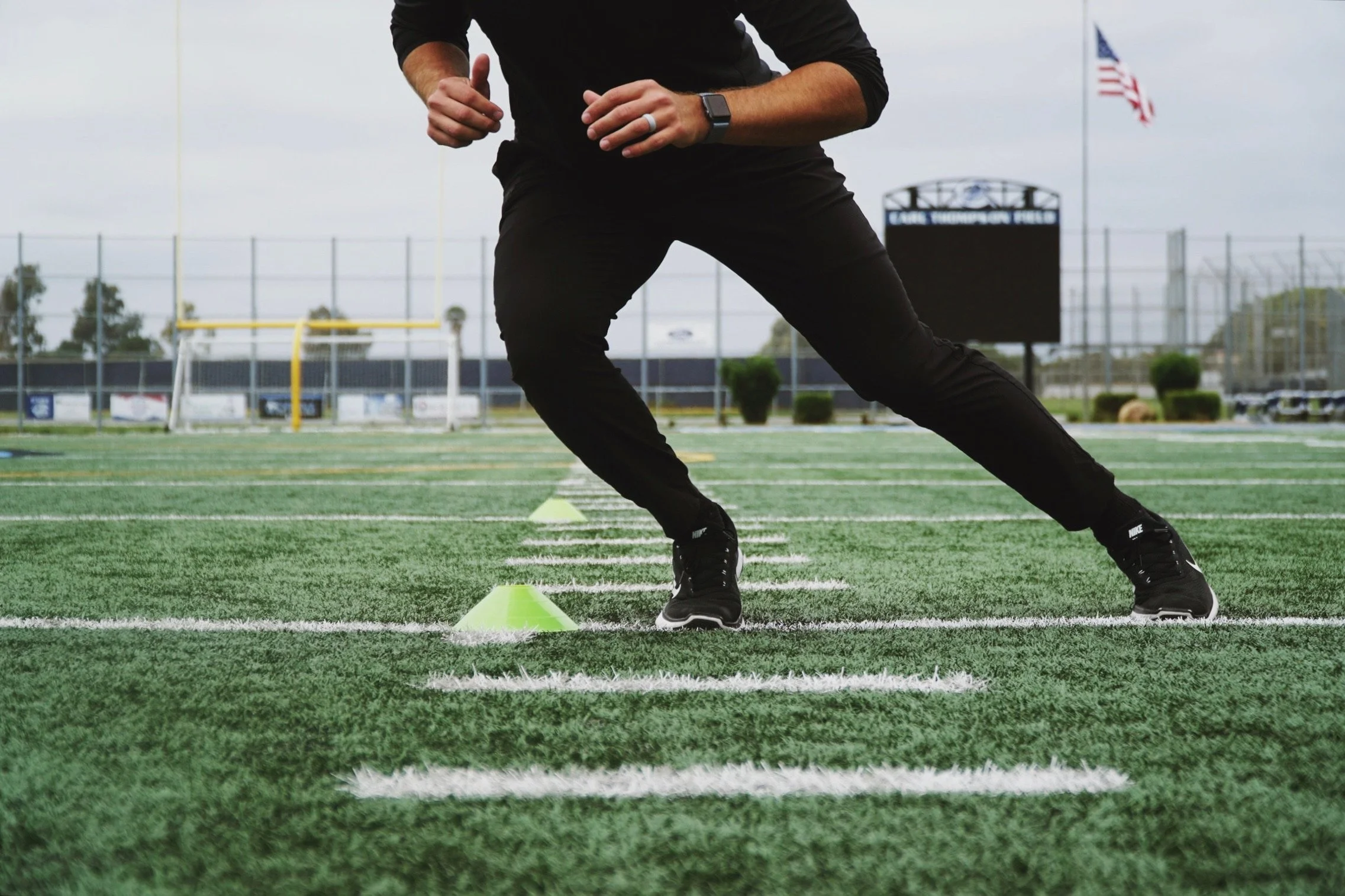 Person in athletic wear performing agility drills on a football field with cones.