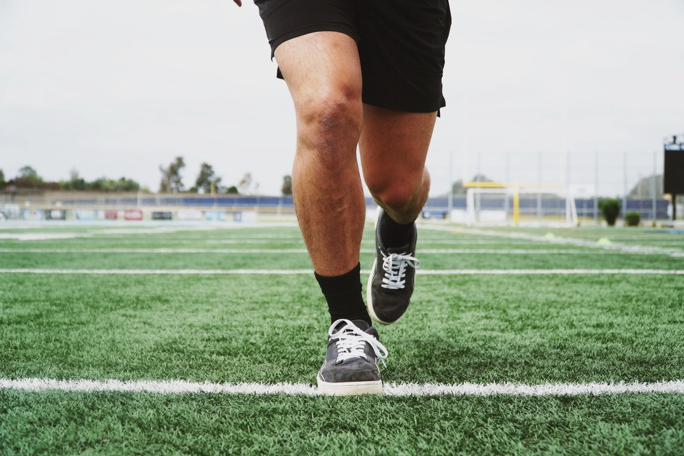 Person running on a football field wearing black shorts and sneakers.