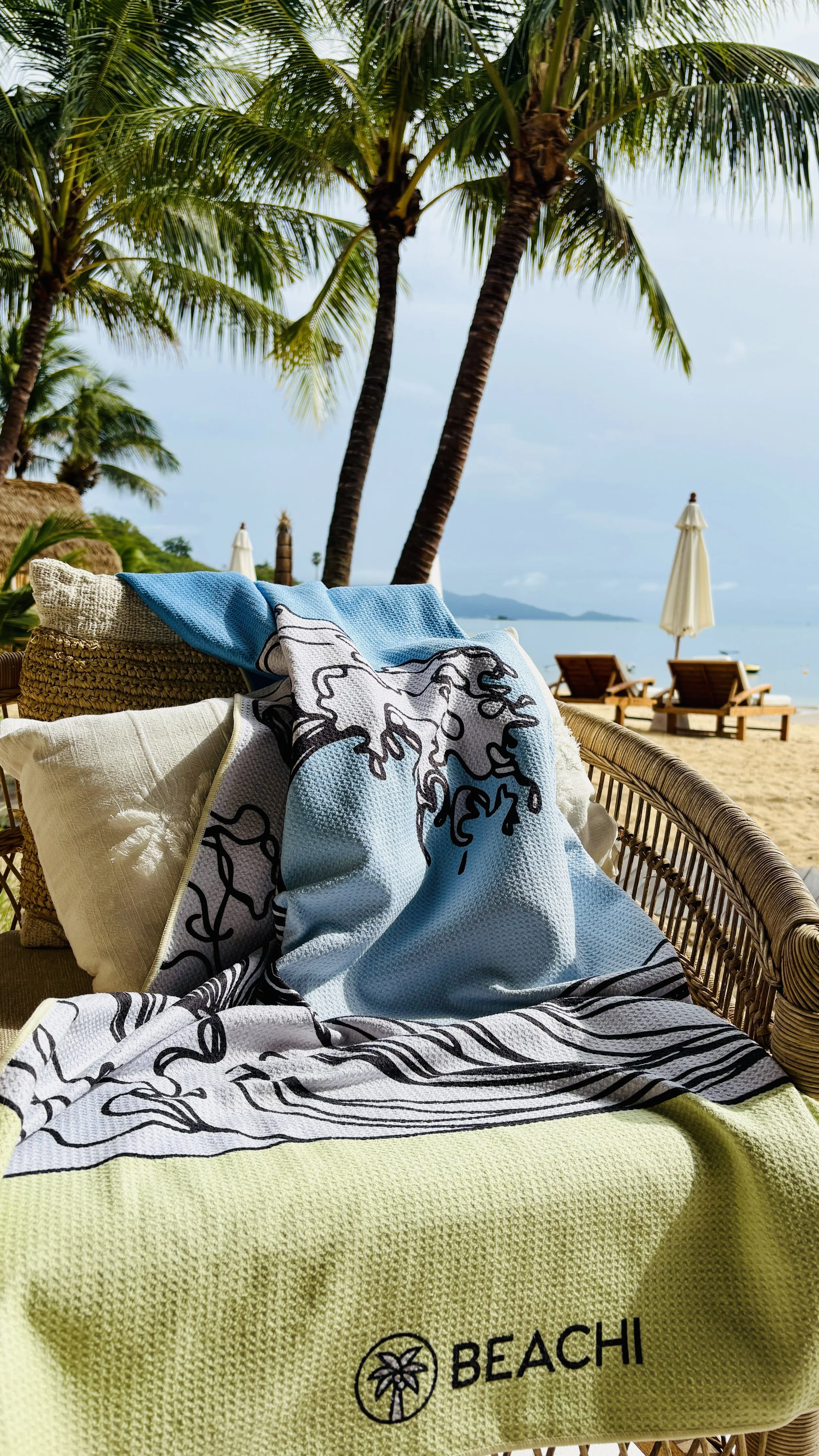 Tropical beach with palm trees, lounge chairs, and umbrellas. Comfortable seating with beach towels and pillows, overlooking the ocean with distant islands.