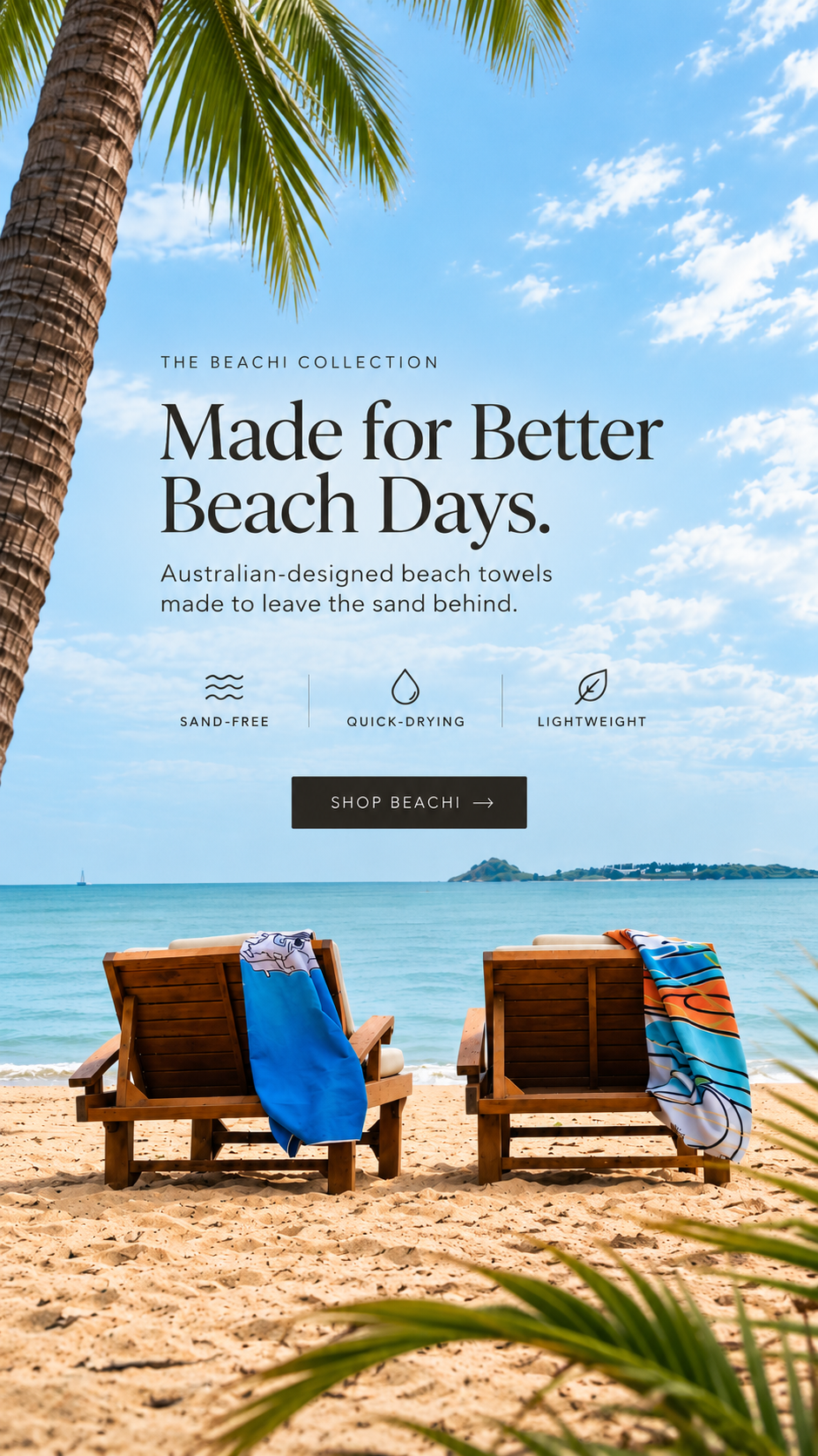 Beach scene with two wooden lounge chairs on sandy shore, colorful BEACHI towels draped over the chairs, palm tree fronds in the foreground, calm ocean and small island in the background, blue sky with clouds.