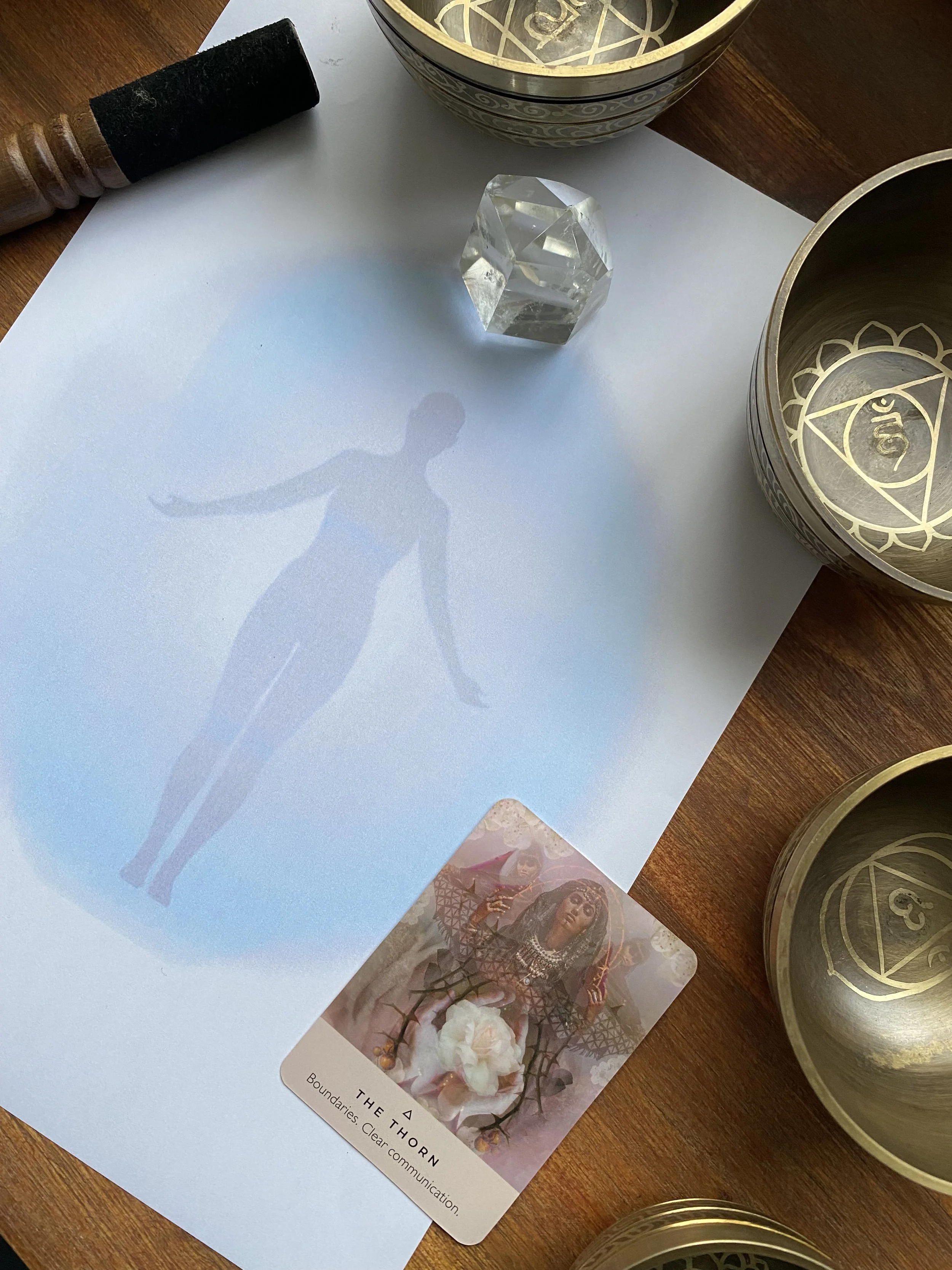A white card with a shadow of a ballerina, a colorful photo of a woman, and a card with flowers and the text 'THE THORN' and 'Boundaries. Clear communication.' on it, along with metallic tins with intricate gold patterns on the table.