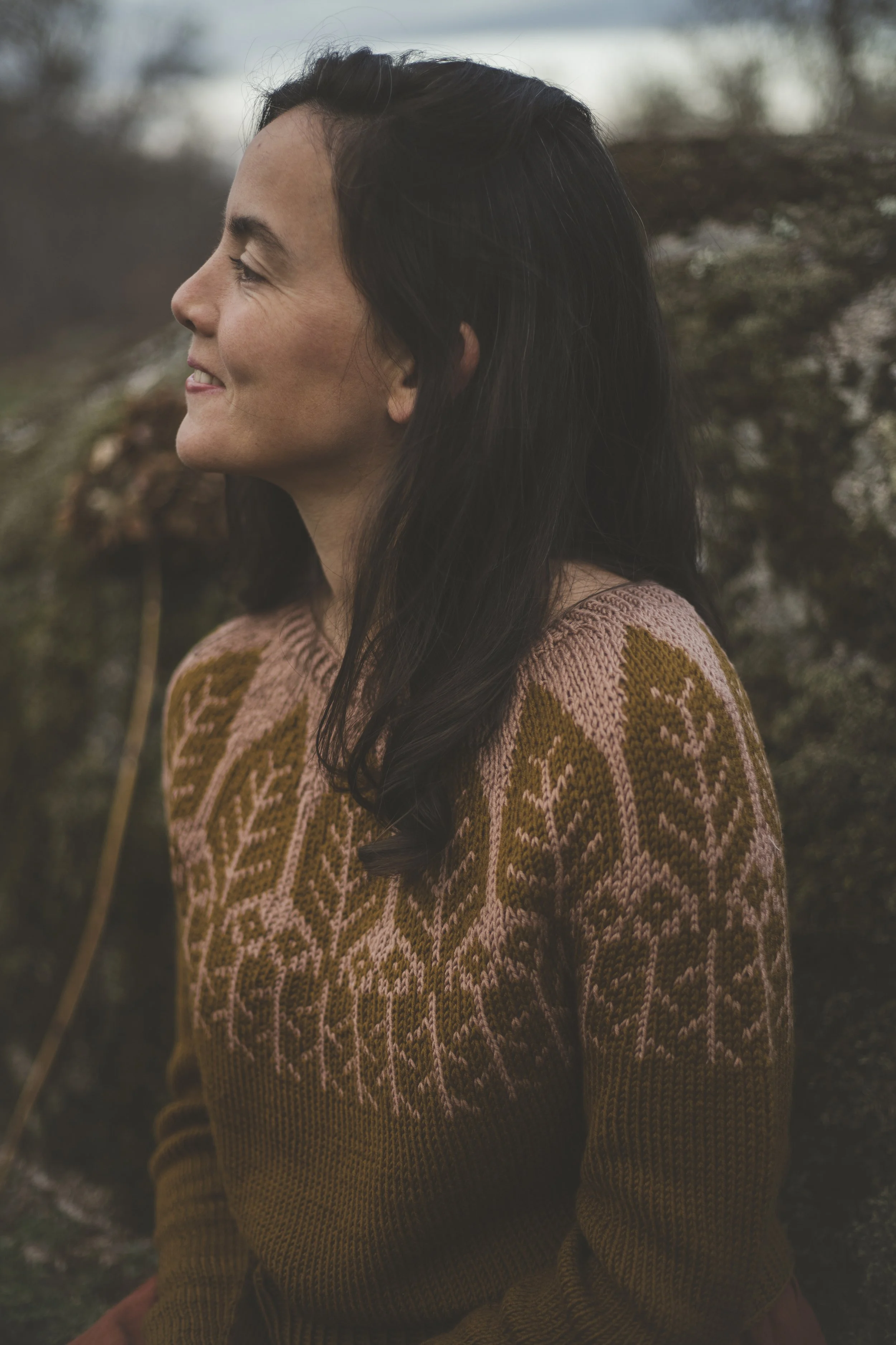 Close-up of hands knitting a brown and beige variegated yarn, with a knitting needle inserted, wearing a beige jacket.