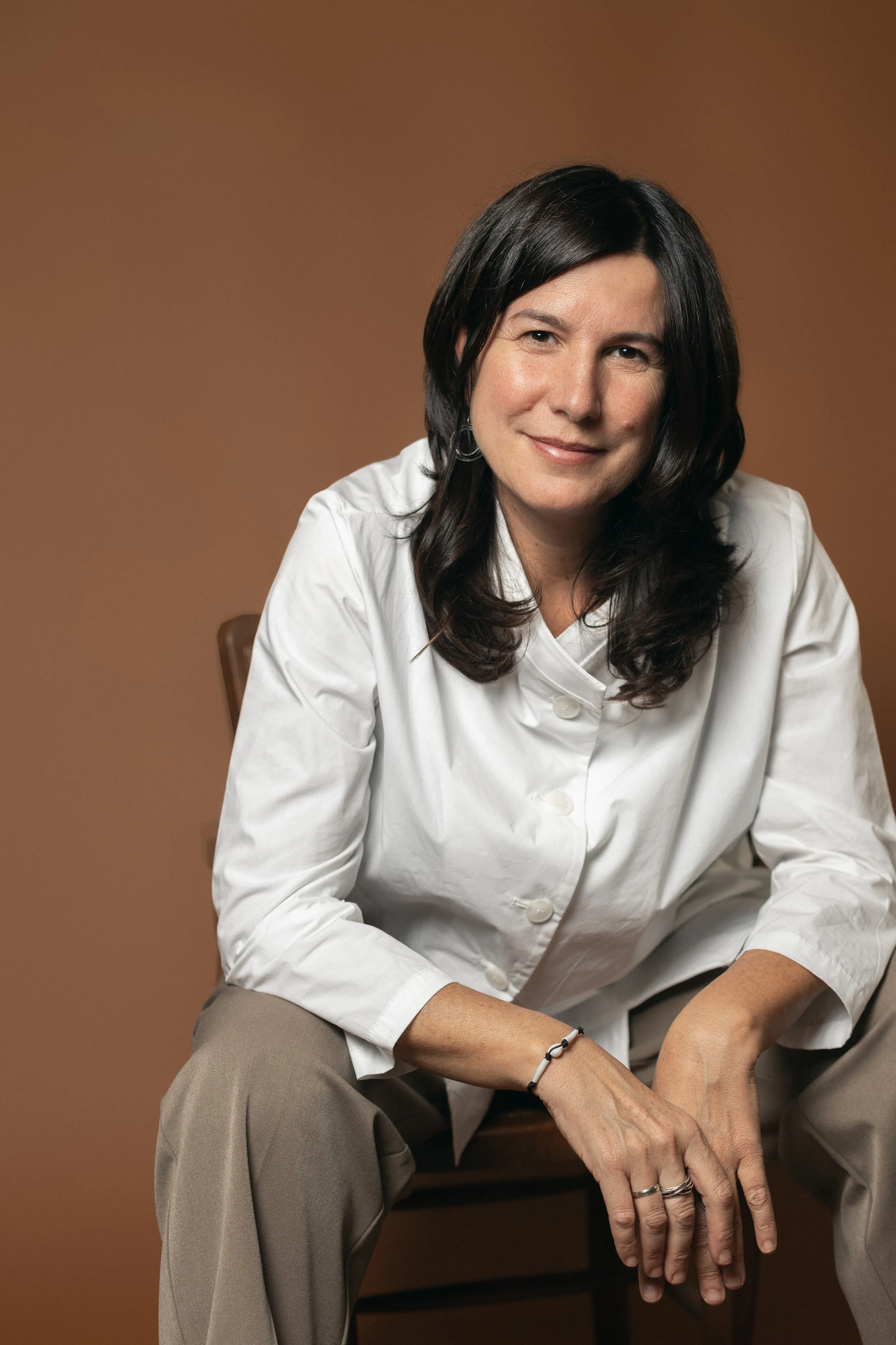 Person stitching brown leather with orange thread using a sewing tool.