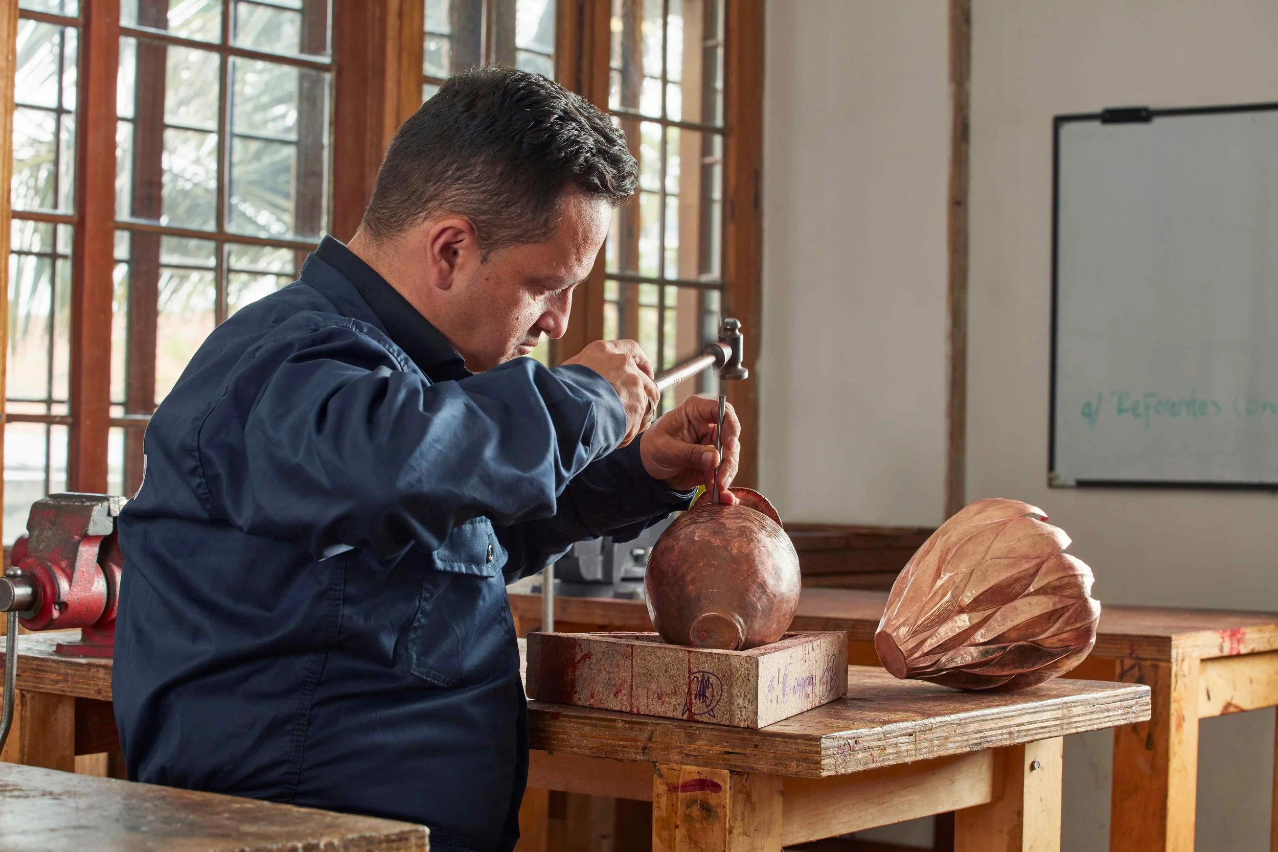 A man working on a wooden sculpture in a workshop, sculpting with a hammer and chisel.