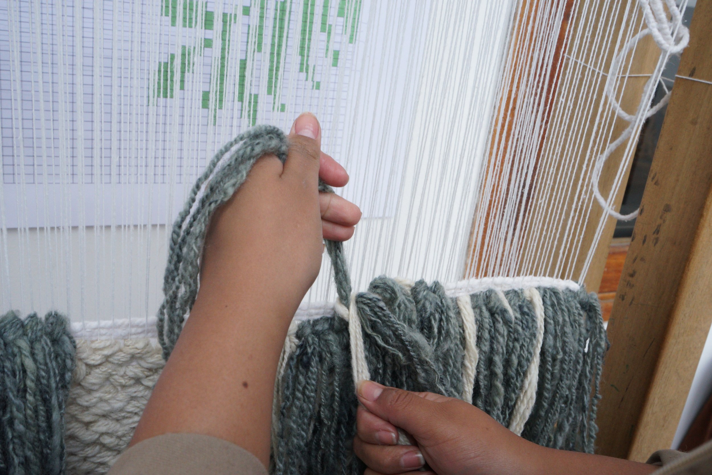 Person weaving fabric on a loom with wooden parts and threads in a workshop.