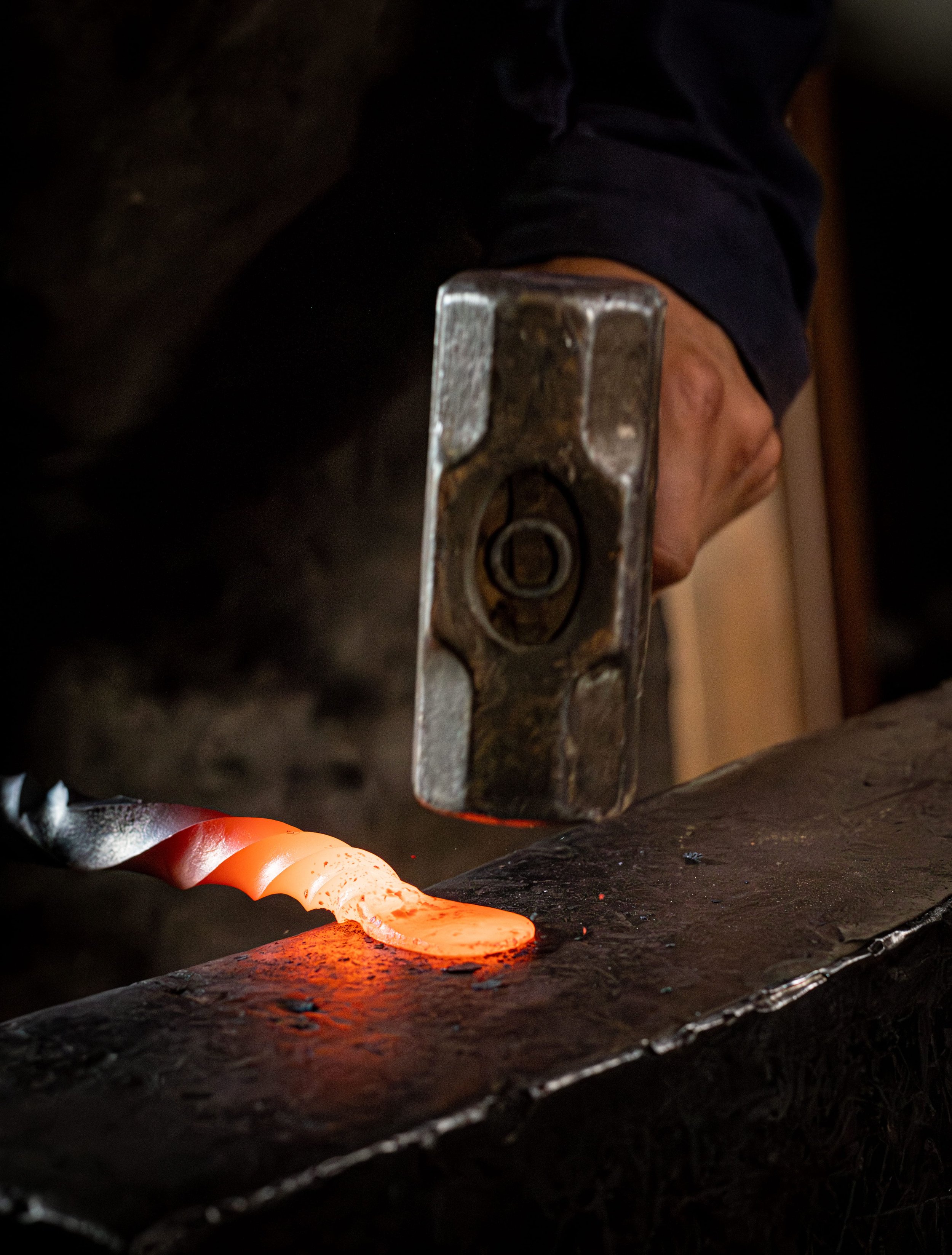 A person wearing a blue jumpsuit hammers a chisel into a large, dark pipe, likely working on pipe repair or maintenance.