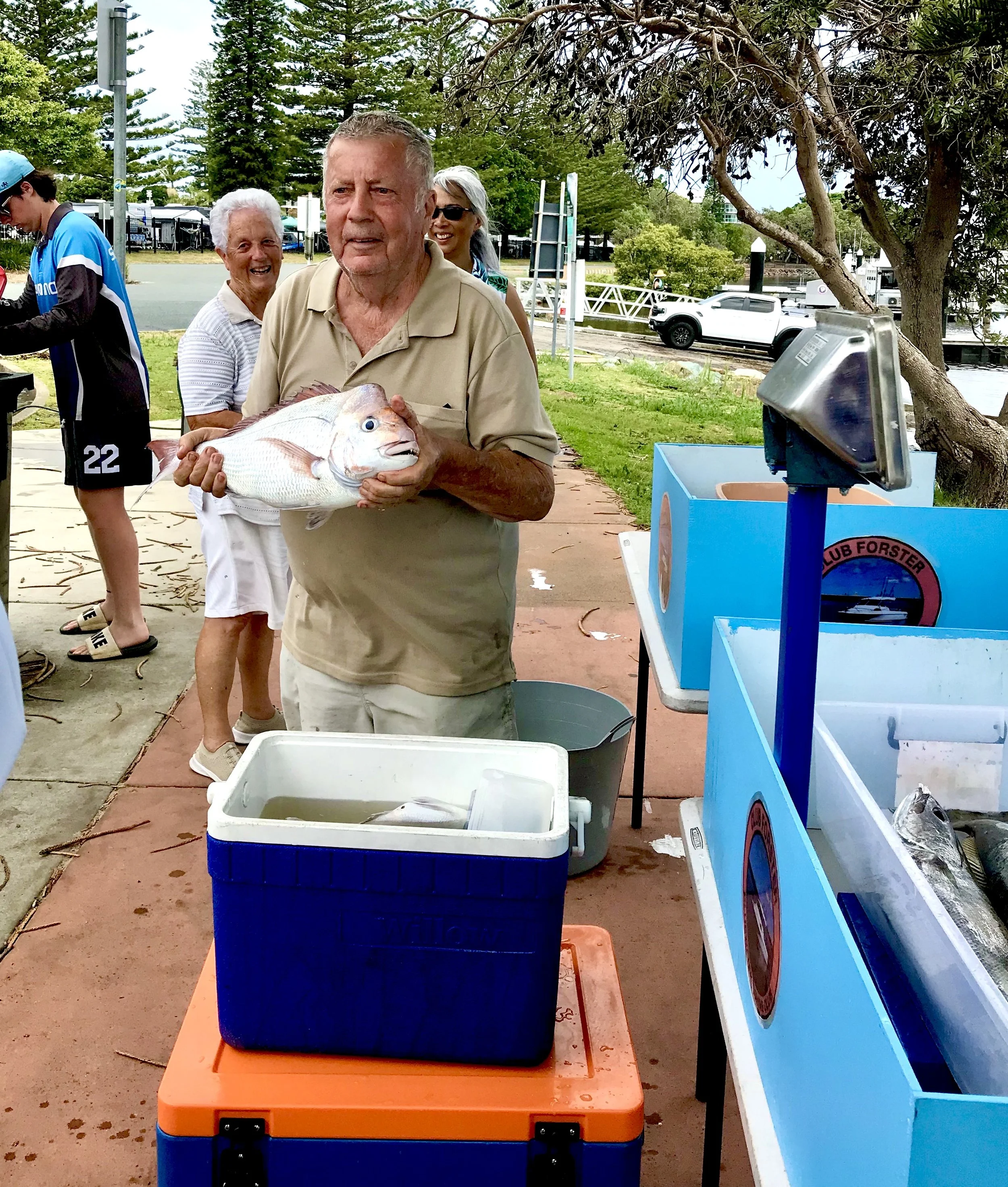 Elderly man holding a large fish near coolers at a fish market.