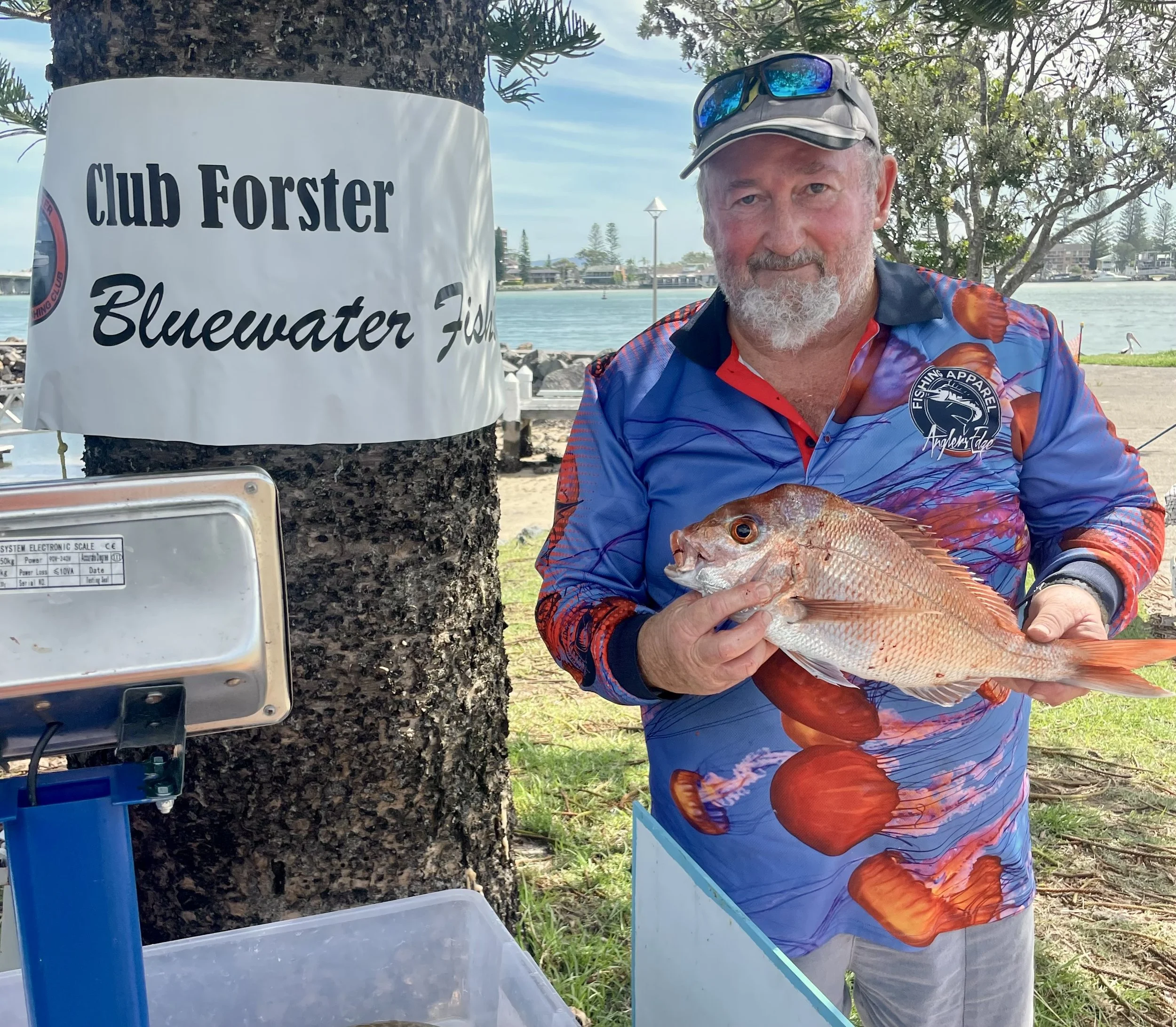 Man holding a fish near a "Club Forster Bluewater Fish" sign.