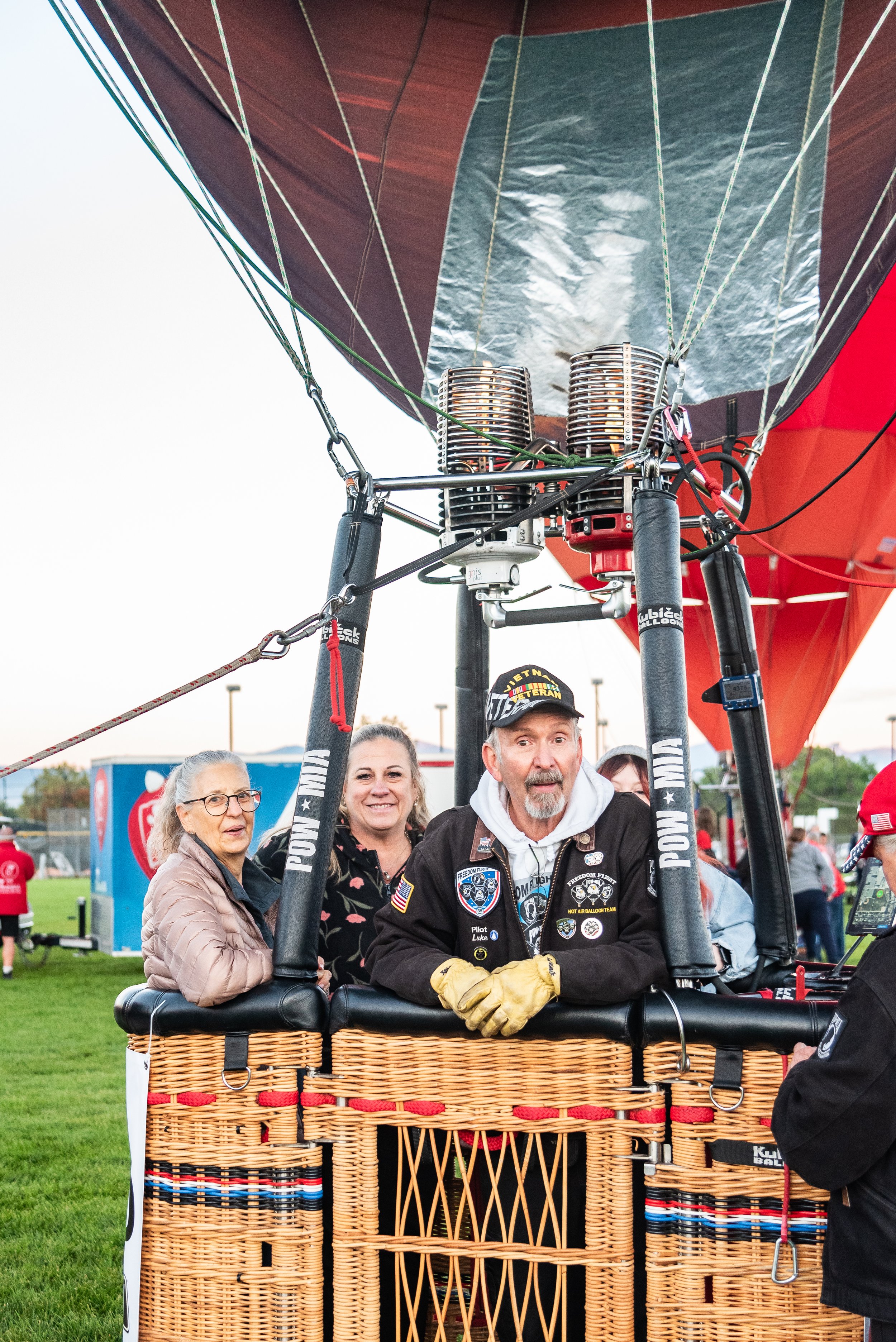 Group of people in a hot air balloon basket preparing for takeoff, featuring a Vietnam veteran with a cap and jacket.