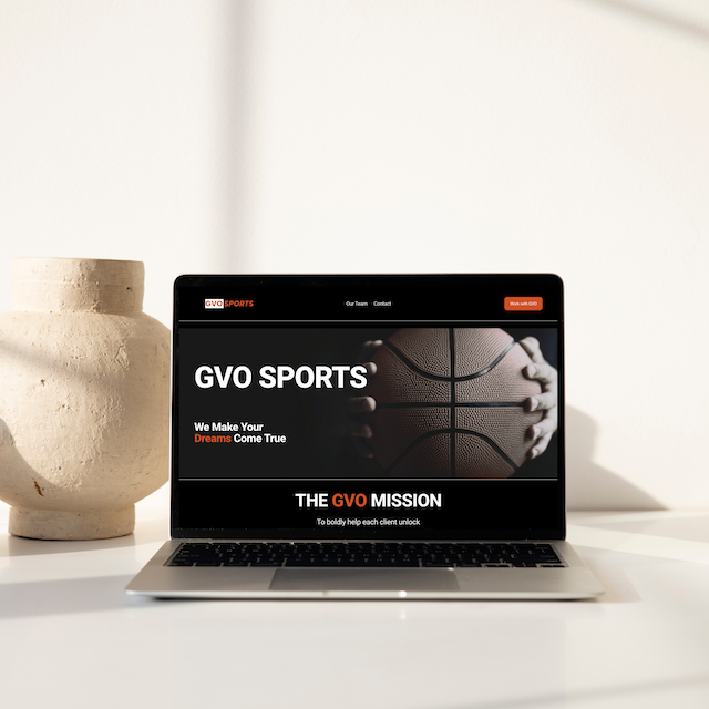 Laptop displaying GVO Sports website with a basketball on the screen, placed on a white desk next to a beige pottery vase.