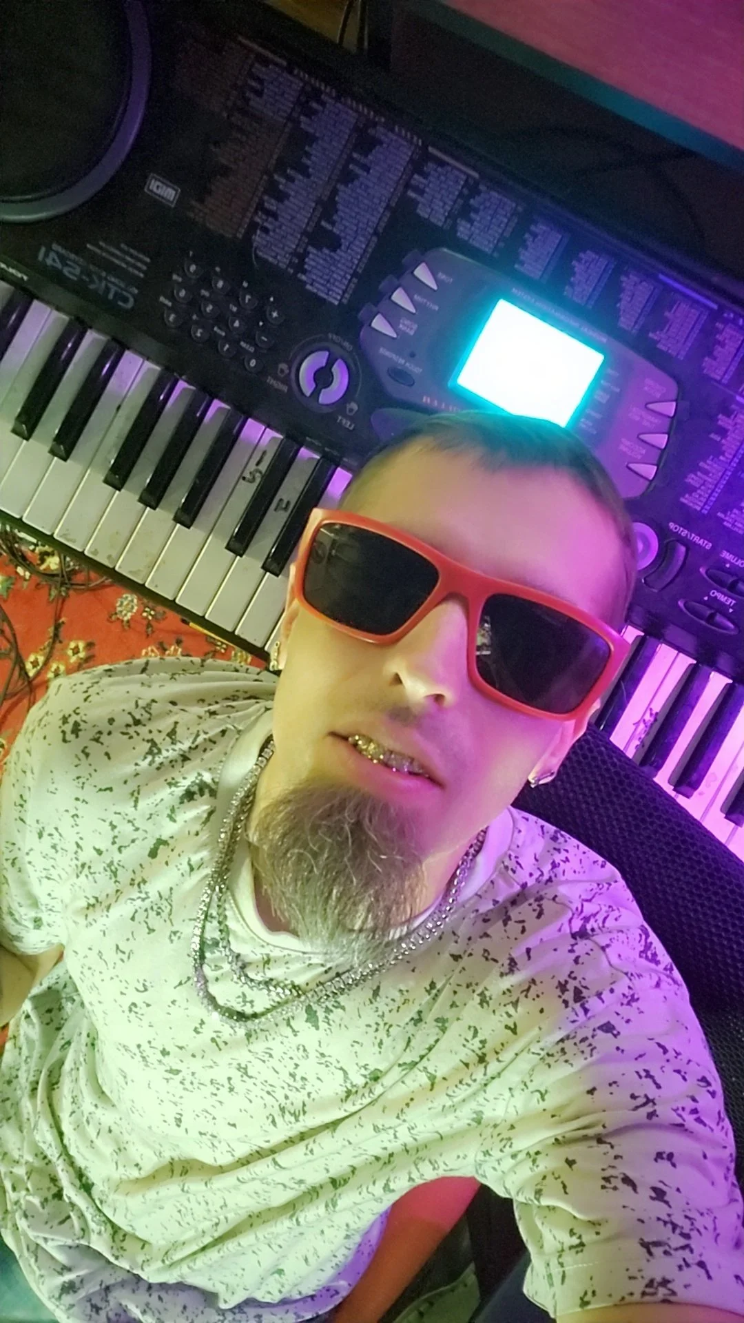 Sundawg taking a selfie in a music studio with a keyboard and a digital music workstation behind them, lit with colorful purple and pink lighting.