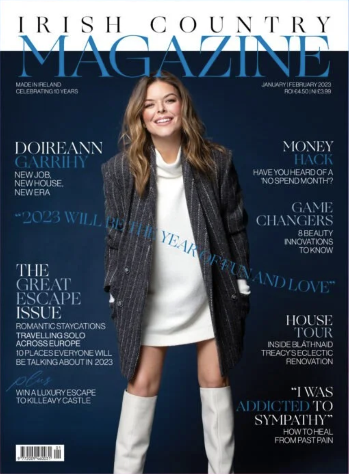 Cover of Irish Country Magazine featuring a smiling woman in a dark plaid blazer, white dress, and white knee-high boots against a dark blue background.