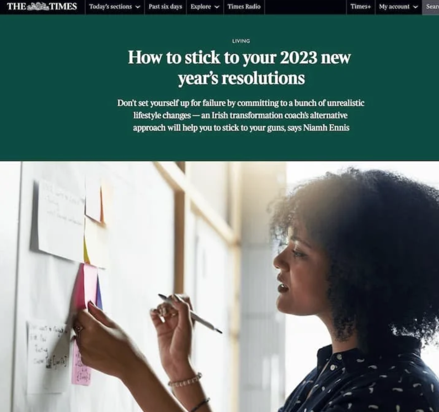 A woman with curly hair writing notes on a whiteboard that has colorful sticky notes on it.