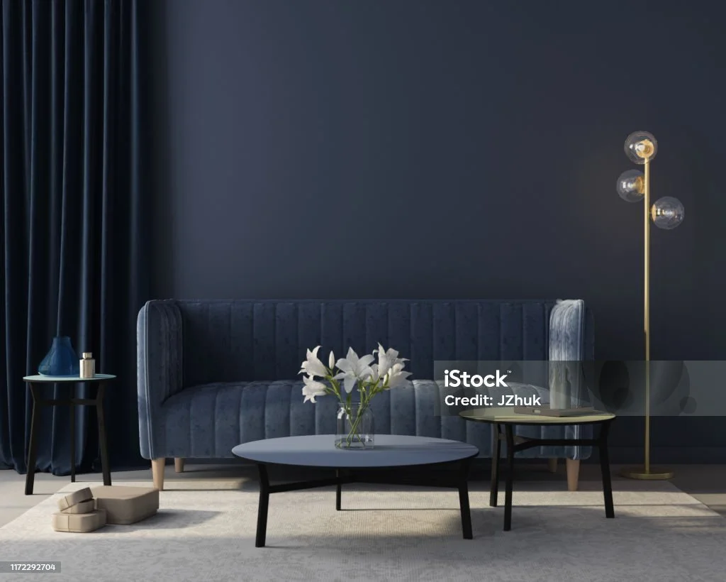Modern living room with dark blue sofa, round coffee tables, white flowers in a vase, gold floor lamp, and dark curtains.