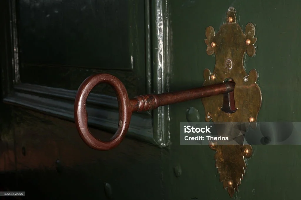 Close-up of an antique skeleton key inserted into an ornate brass keyhole on a dark green wooden door.
