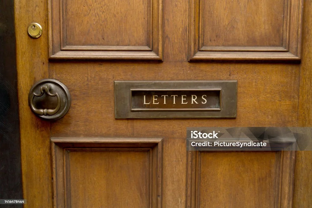 Close-up of a wooden door with a brass mail slot labeled 'LETTERS' and a round doorknob.