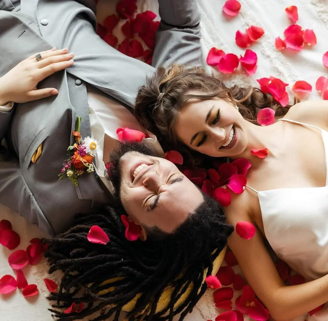 A happy couple lying on a bed with pink rose petals scattered around, smiling and enjoying each other's company.