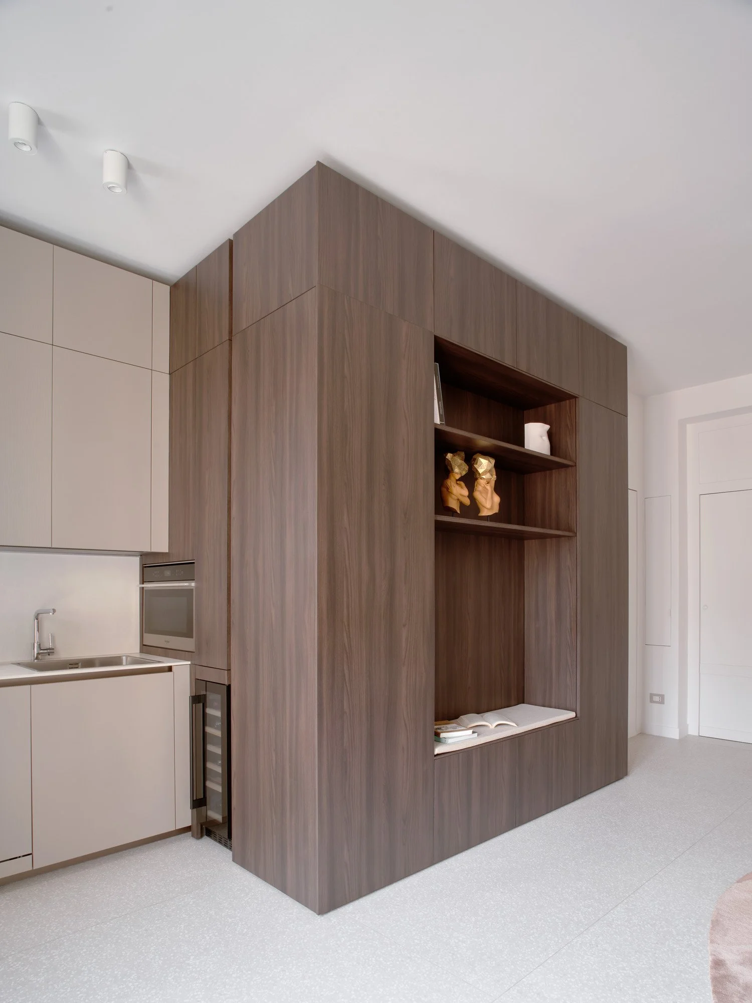 Angolo di una cucina moderna con armadietti beige e una parete in legno scuro con mensole e oggetti decorativi.