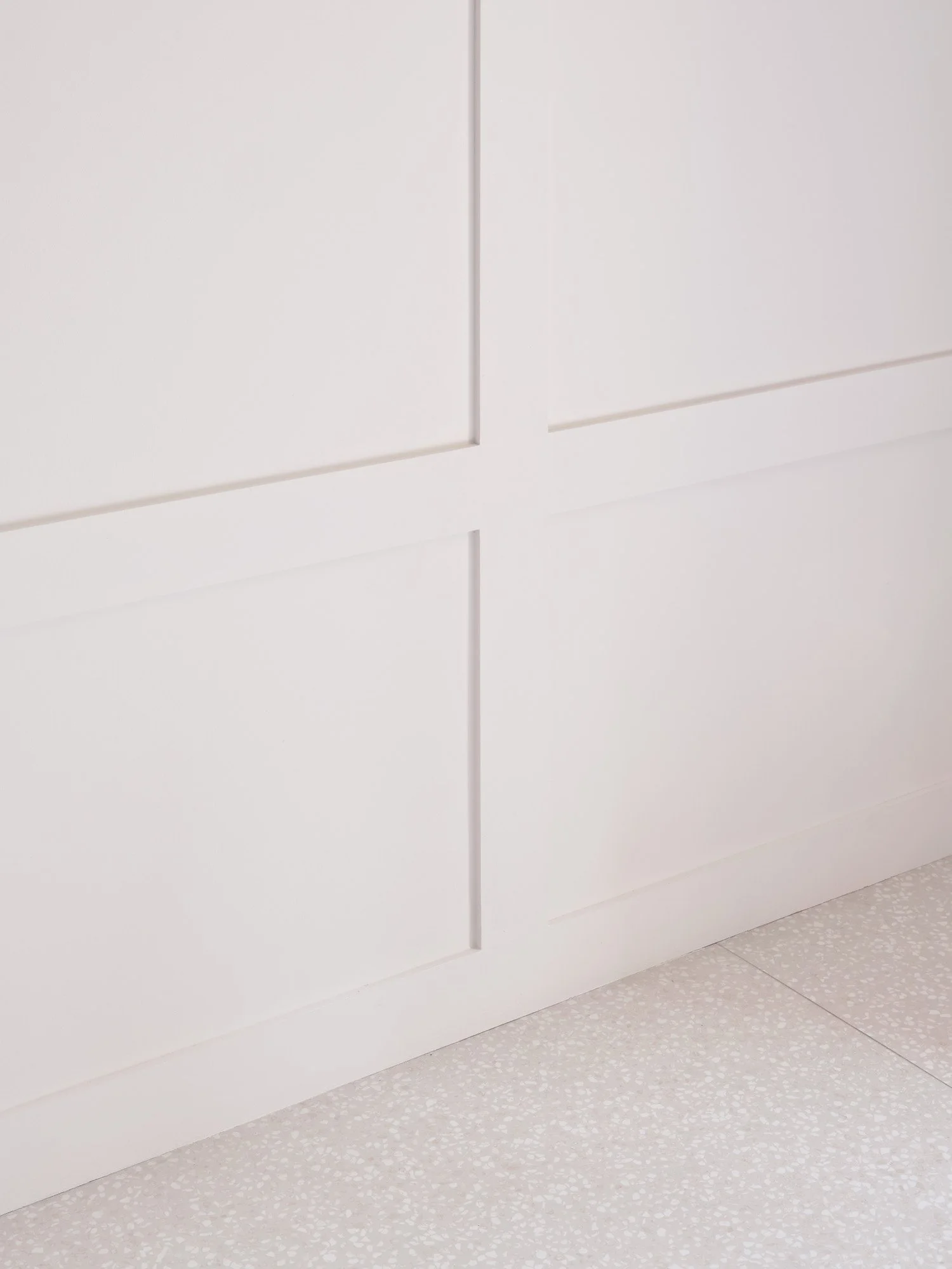 Muro bianco con pannelli e base in legno, pavimento in piastrelle bianche con piccoli motivi