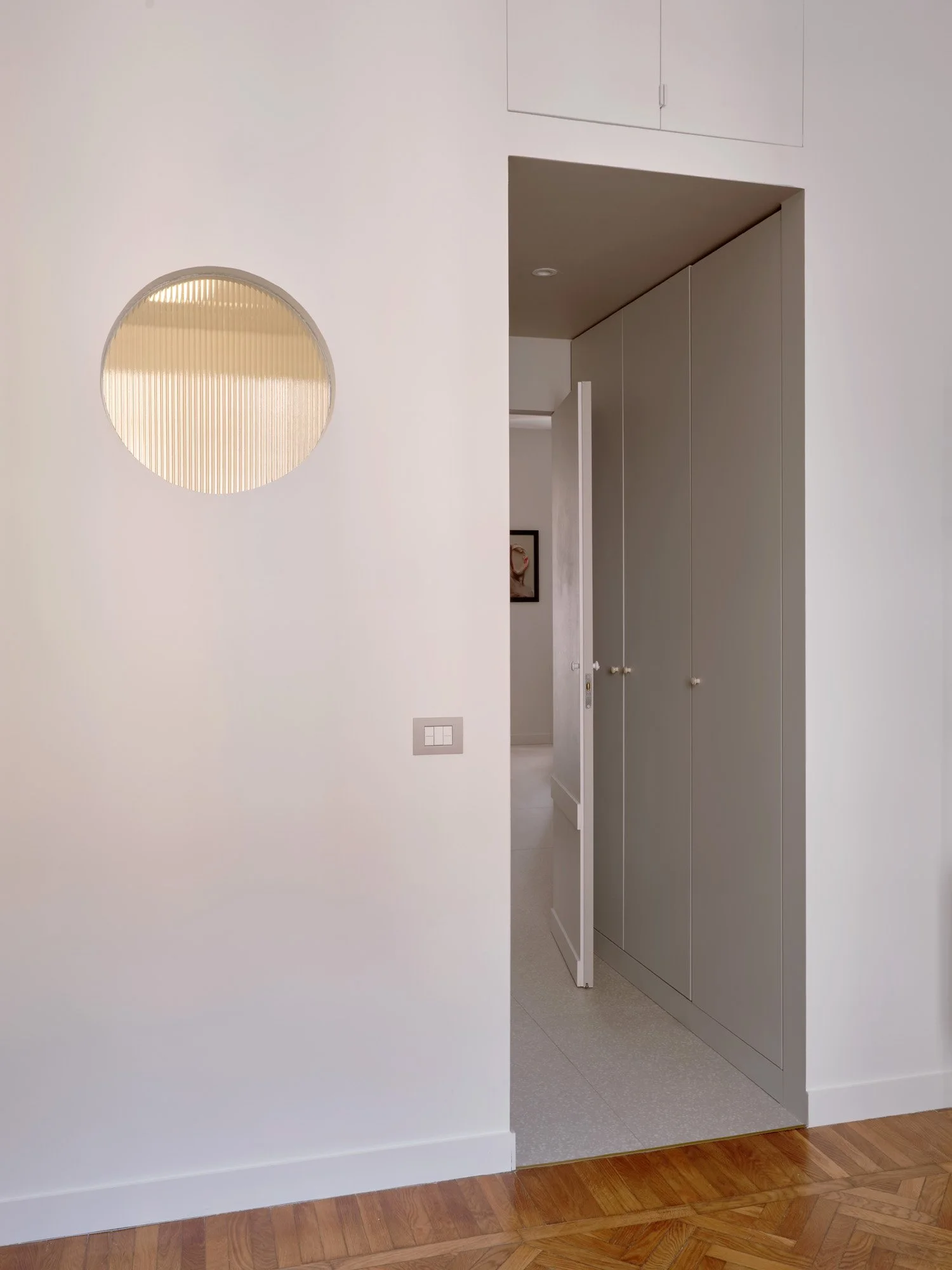 Design interno di un corridoio con parete bianca, porta aperta, armadio grigio e pavimento in parquet